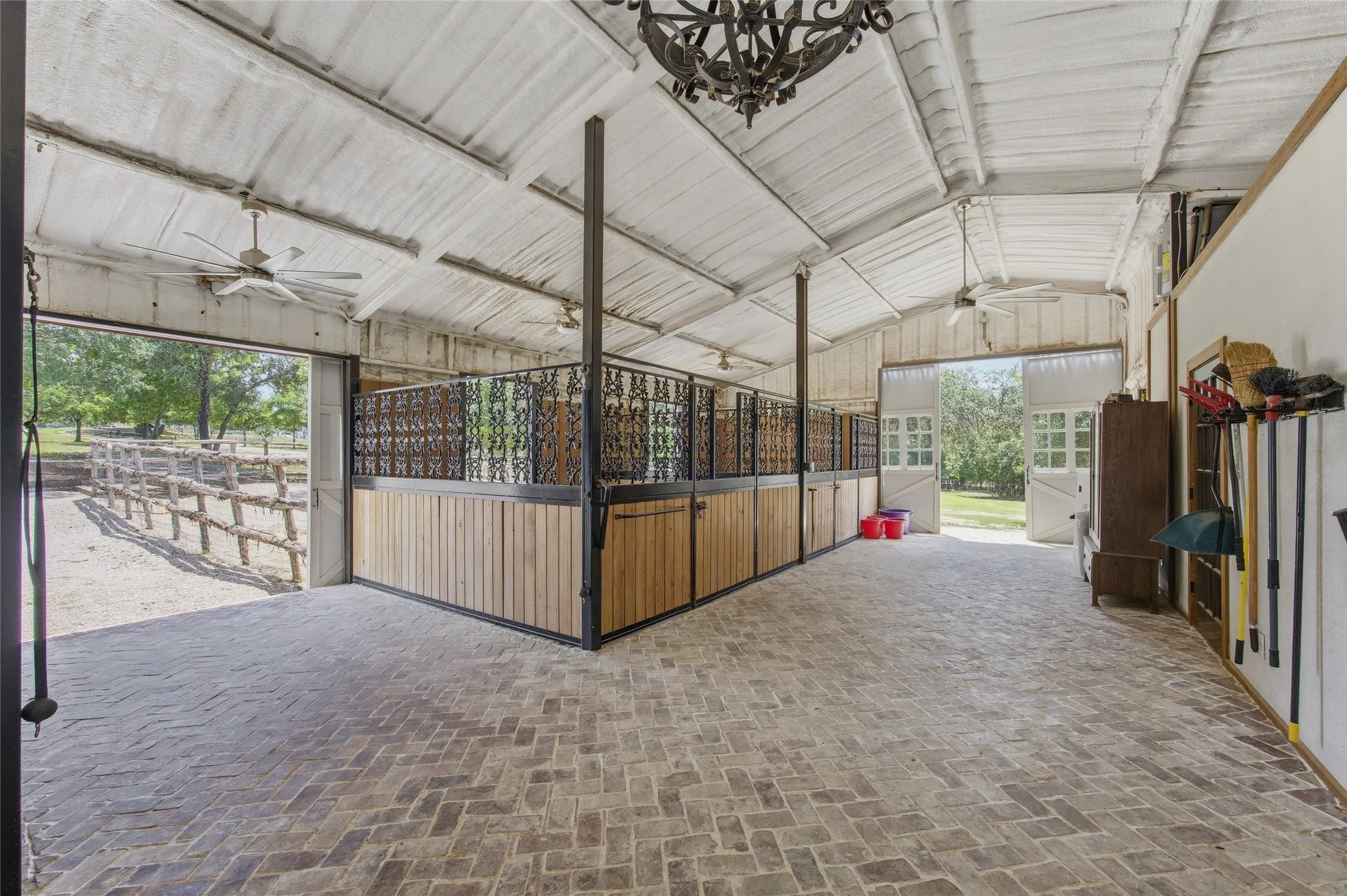 Barn structure featuring brick flooring, wood-paneled stalls with decorative metal work, and exposed beam ceilings with ceiling fans