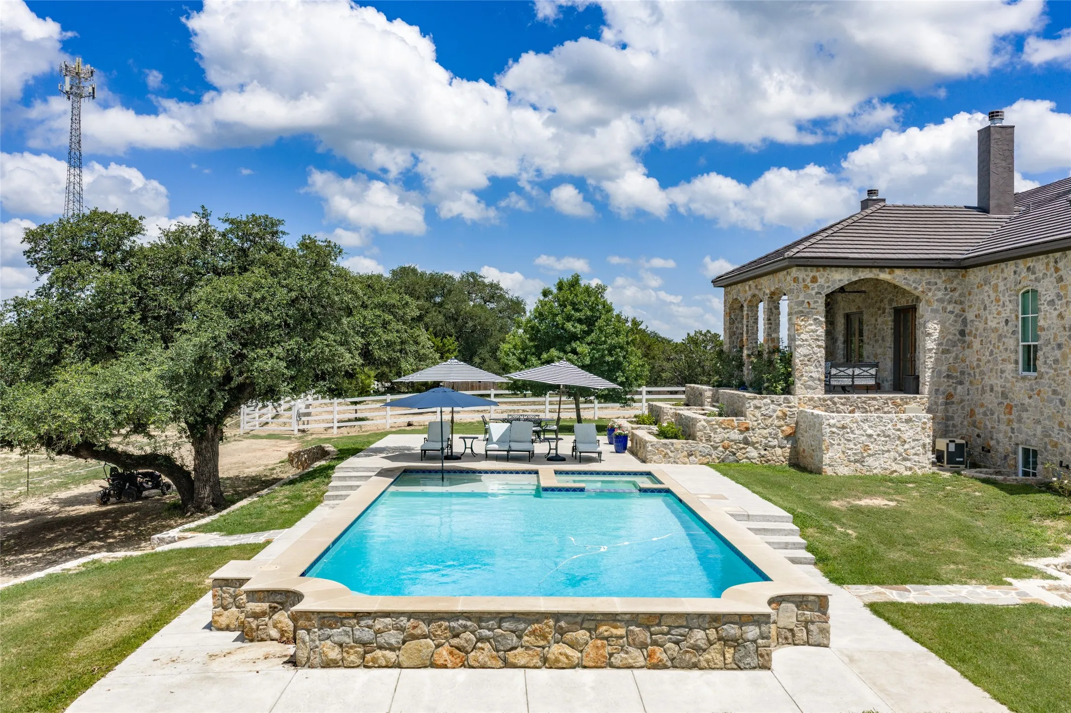 Stone exterior property with a rectangular swimming pool, stone retaining walls, and a covered patio