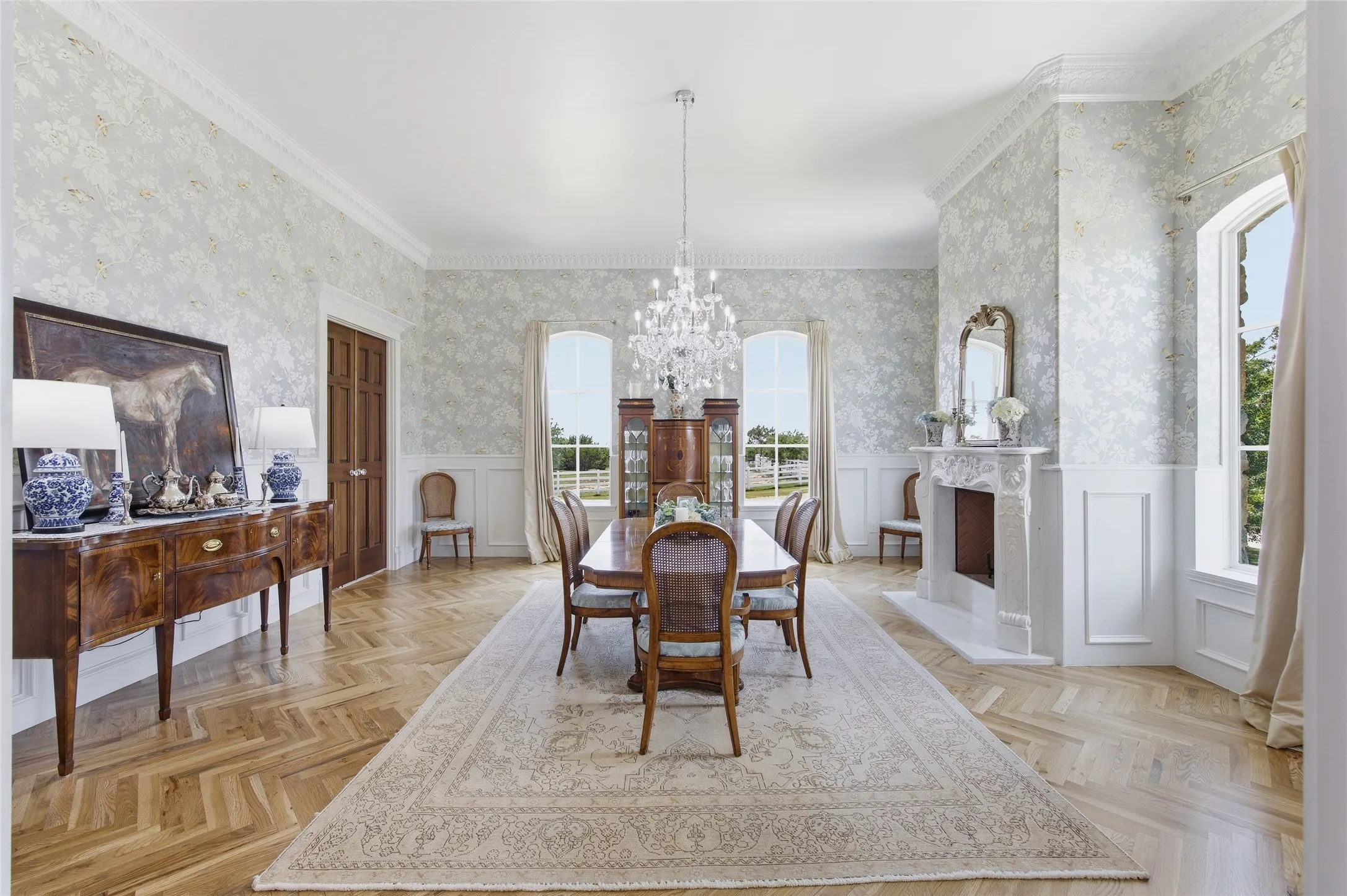 Herringbone wood-finish flooring, ornate chandelier, decorative fireplace, paneled wainscoting, and large windows