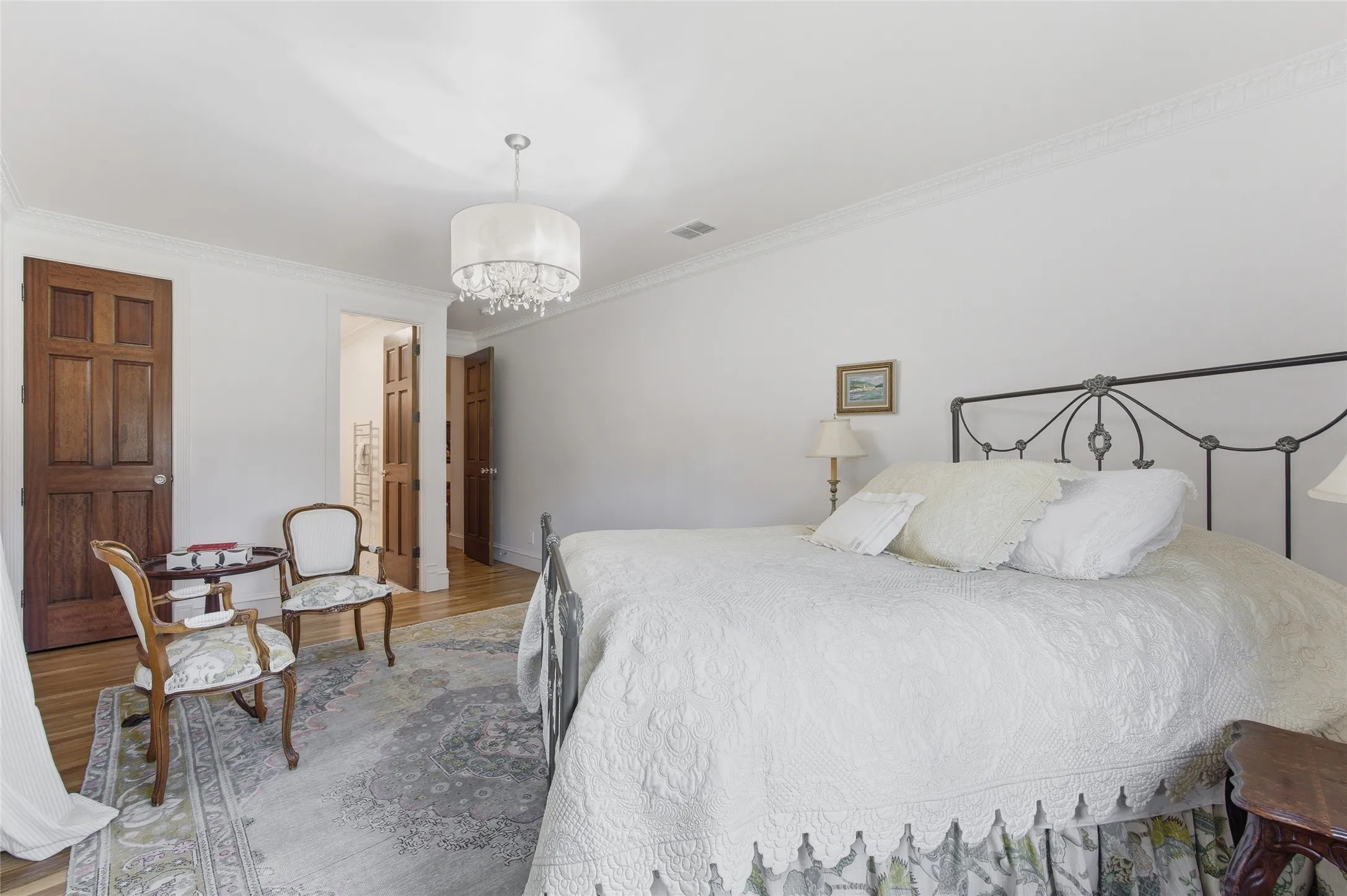 Hardwood flooring with a decorative area rug, crown molding, and a drum-shaped chandelier