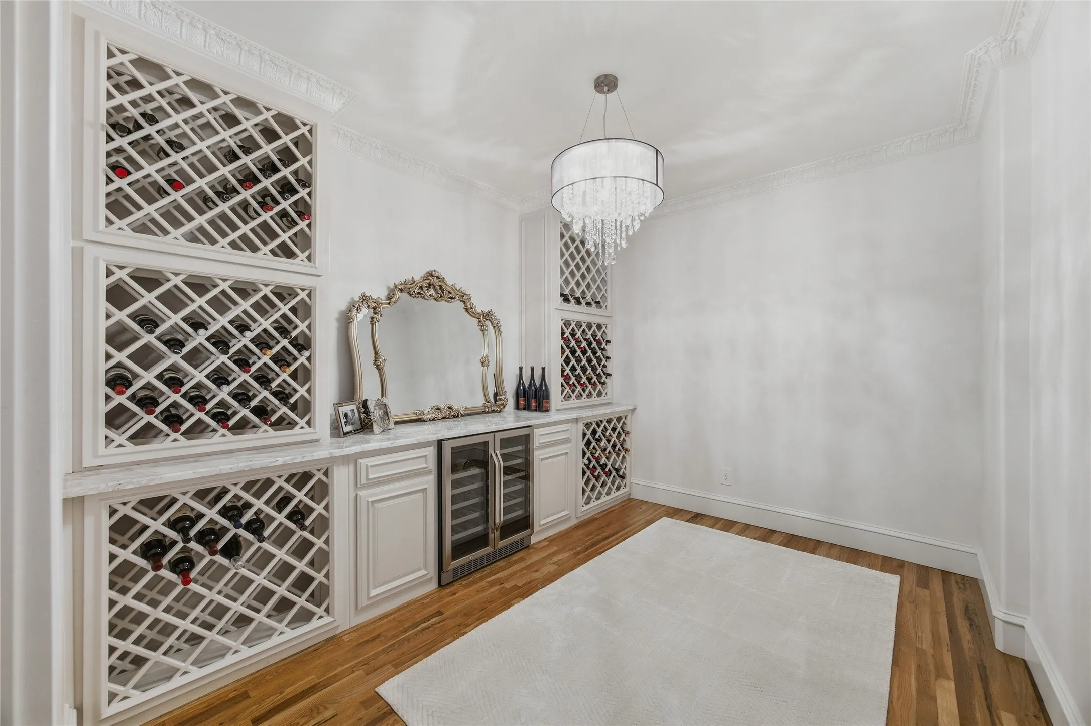 Custom built-in wine storage with integrated beverage cooler, natural wood-finish flooring, and a contemporary crystal chandelier