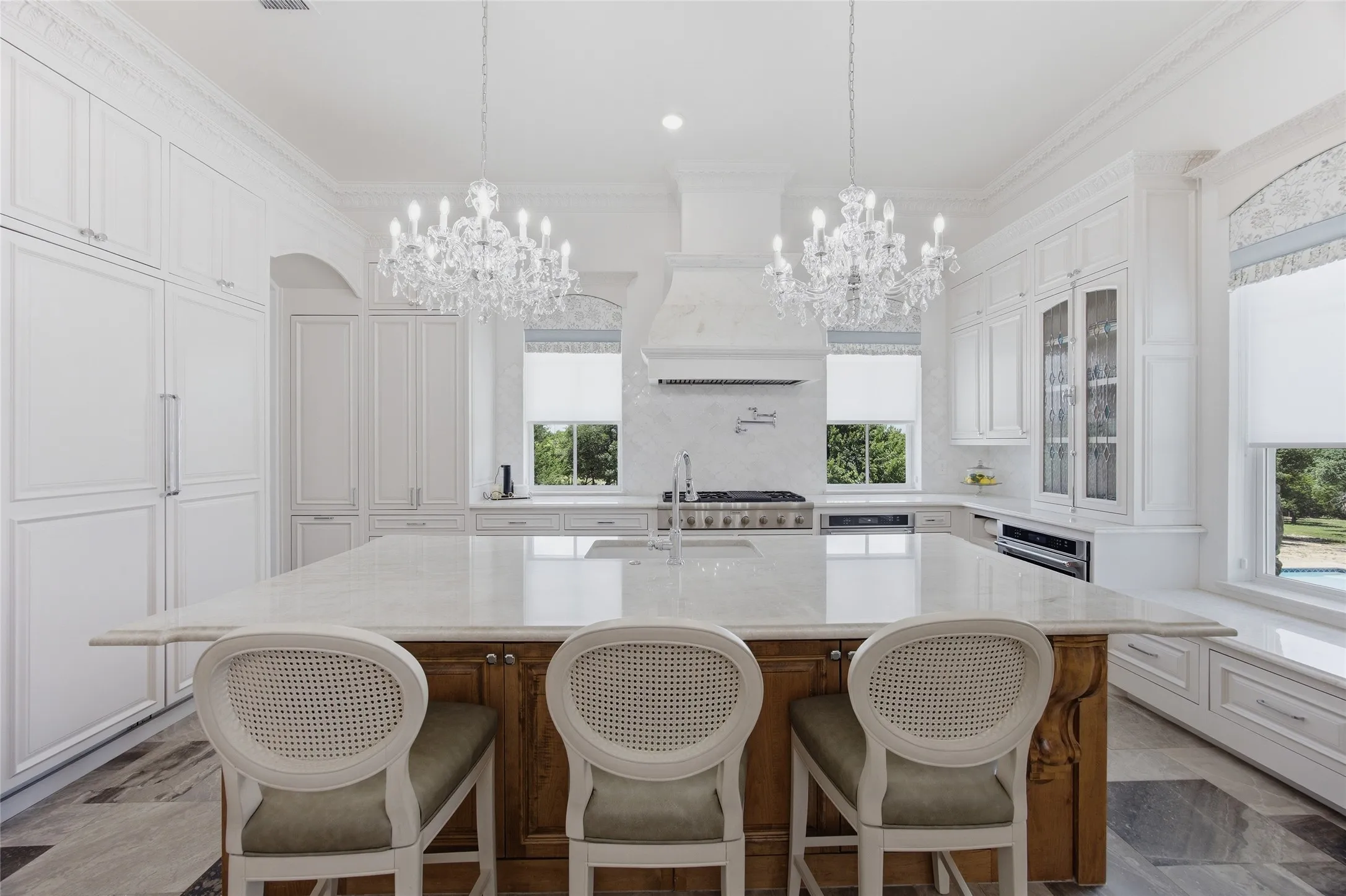 Gourmet kitchen featuring a large central island with seating, integrated paneled appliances, ornate crystal chandeliers, custom cabinetry, and a built-in window seat