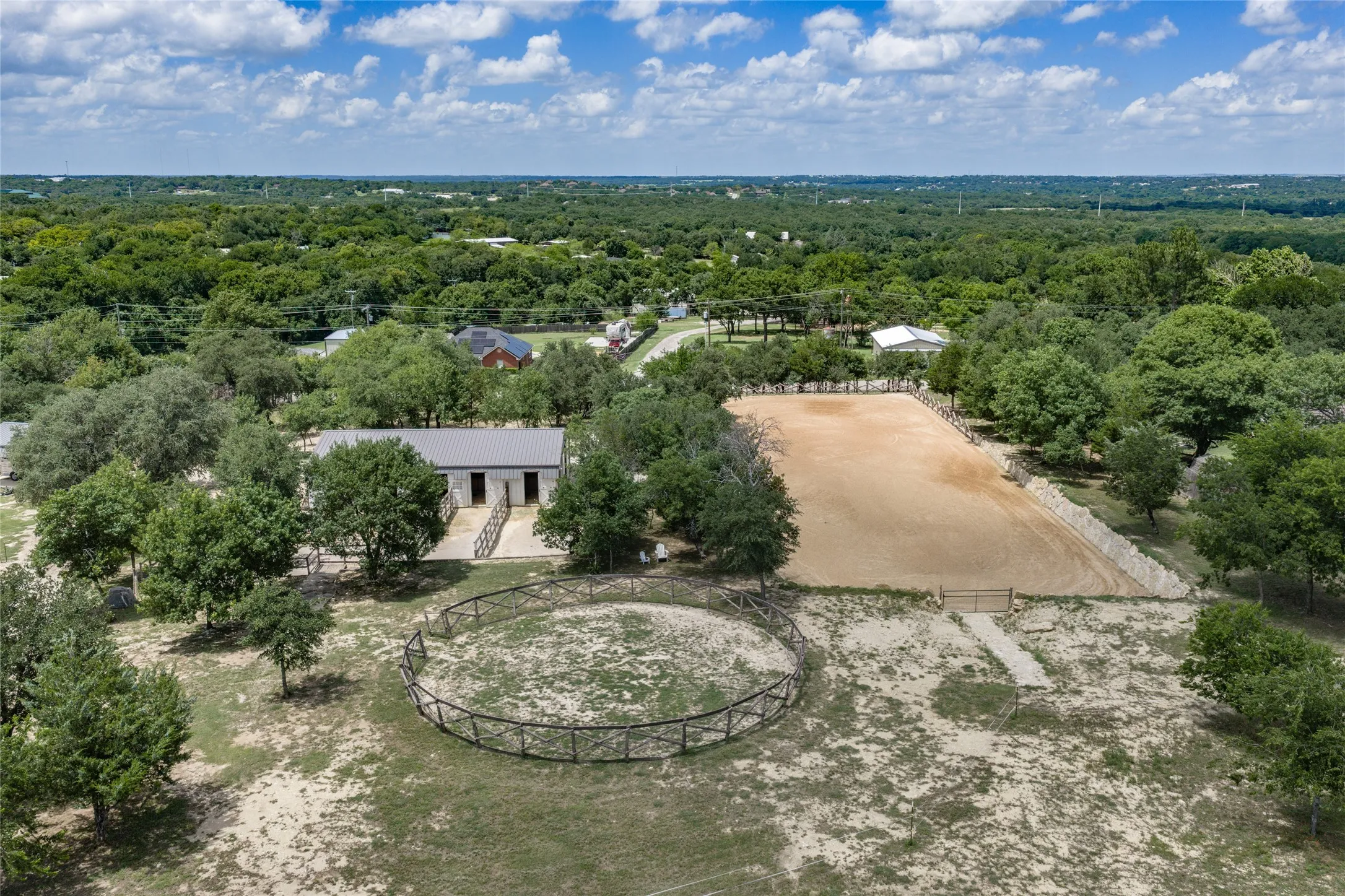 Equestrian property featuring a barn, round pen, and a large riding arena surrounded by mature trees