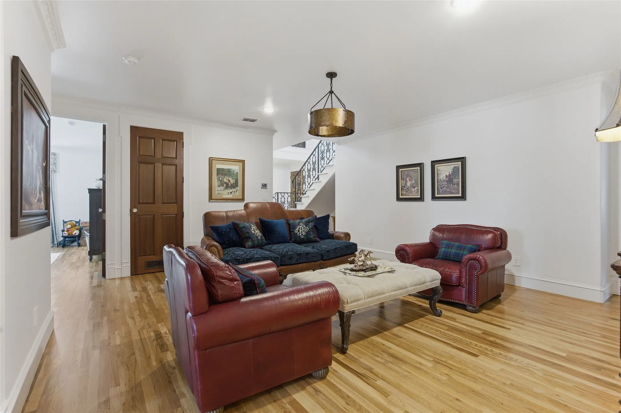 Hardwood flooring, crown molding, a paneled door, a decorative chandelier, and an iron staircase railing