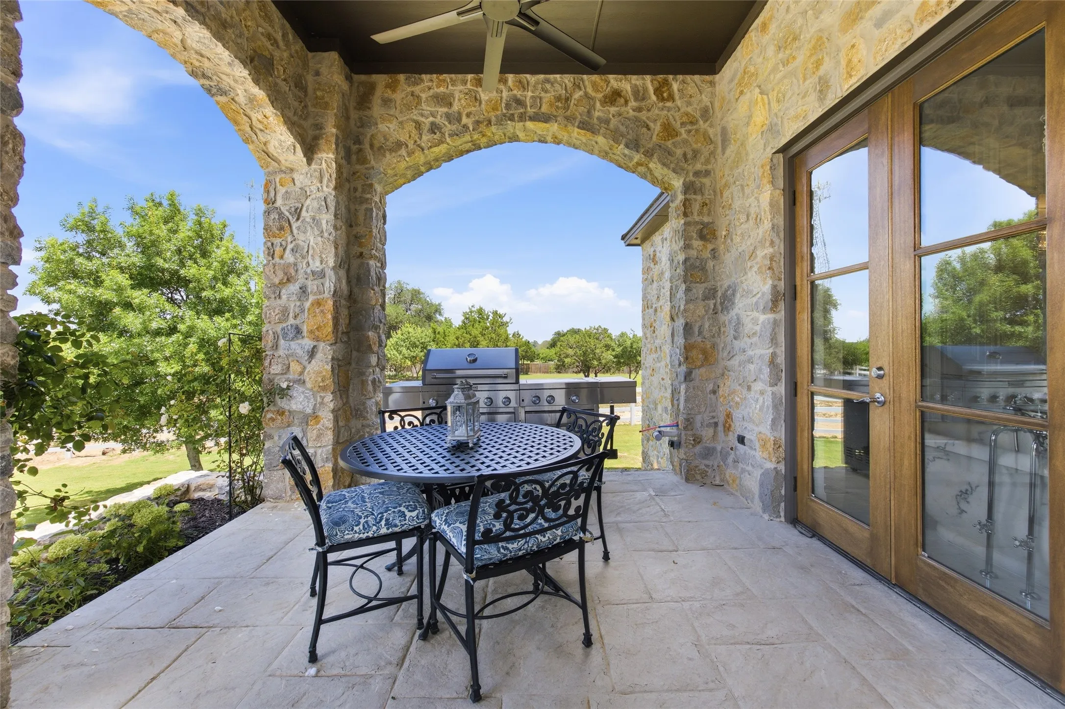 Stone-clad patio with arched openings, stone tile flooring, and a built-in outdoor grill