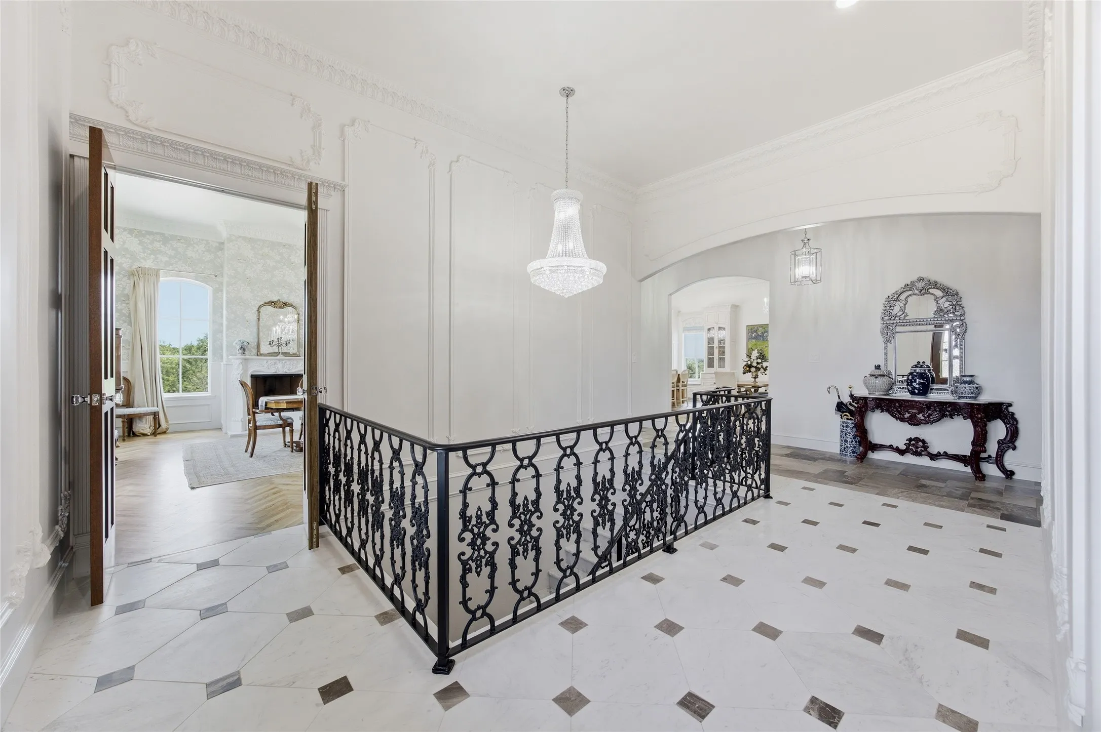Ornate wrought iron railing, decorative ceiling molding, crystal chandelier, tile flooring with inset accents, and arched entryways