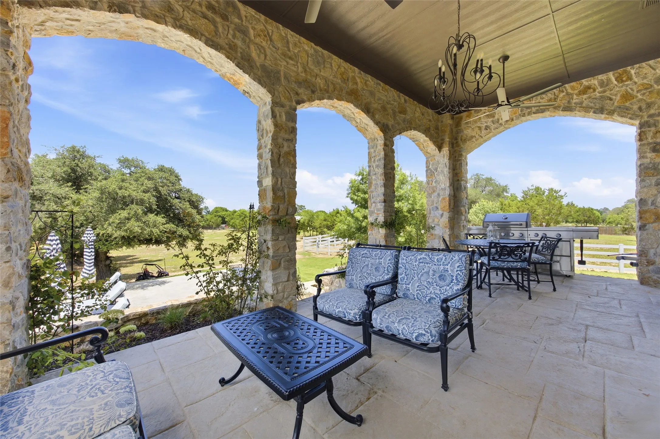 Expansive covered patio featuring stone archways, integrated outdoor kitchen, stone flooring, and an ornamental chandelier