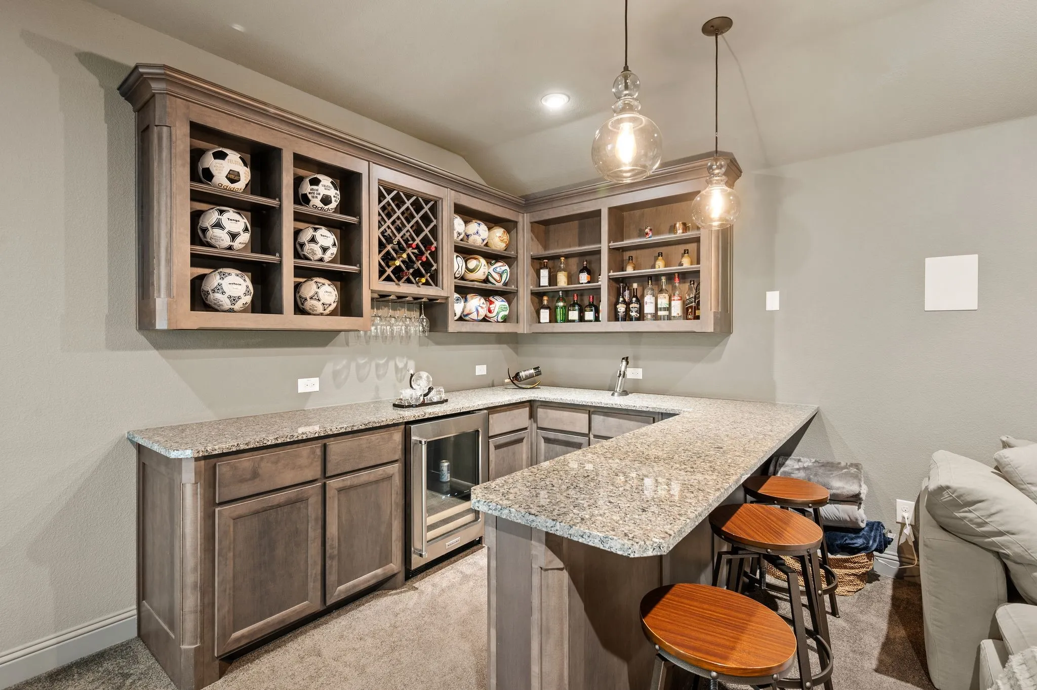 Sophisticated bar featuring custom wood-finish cabinetry with open shelving for curated display, quartz countertops, a built-in beverage cooler, and pendant lighting