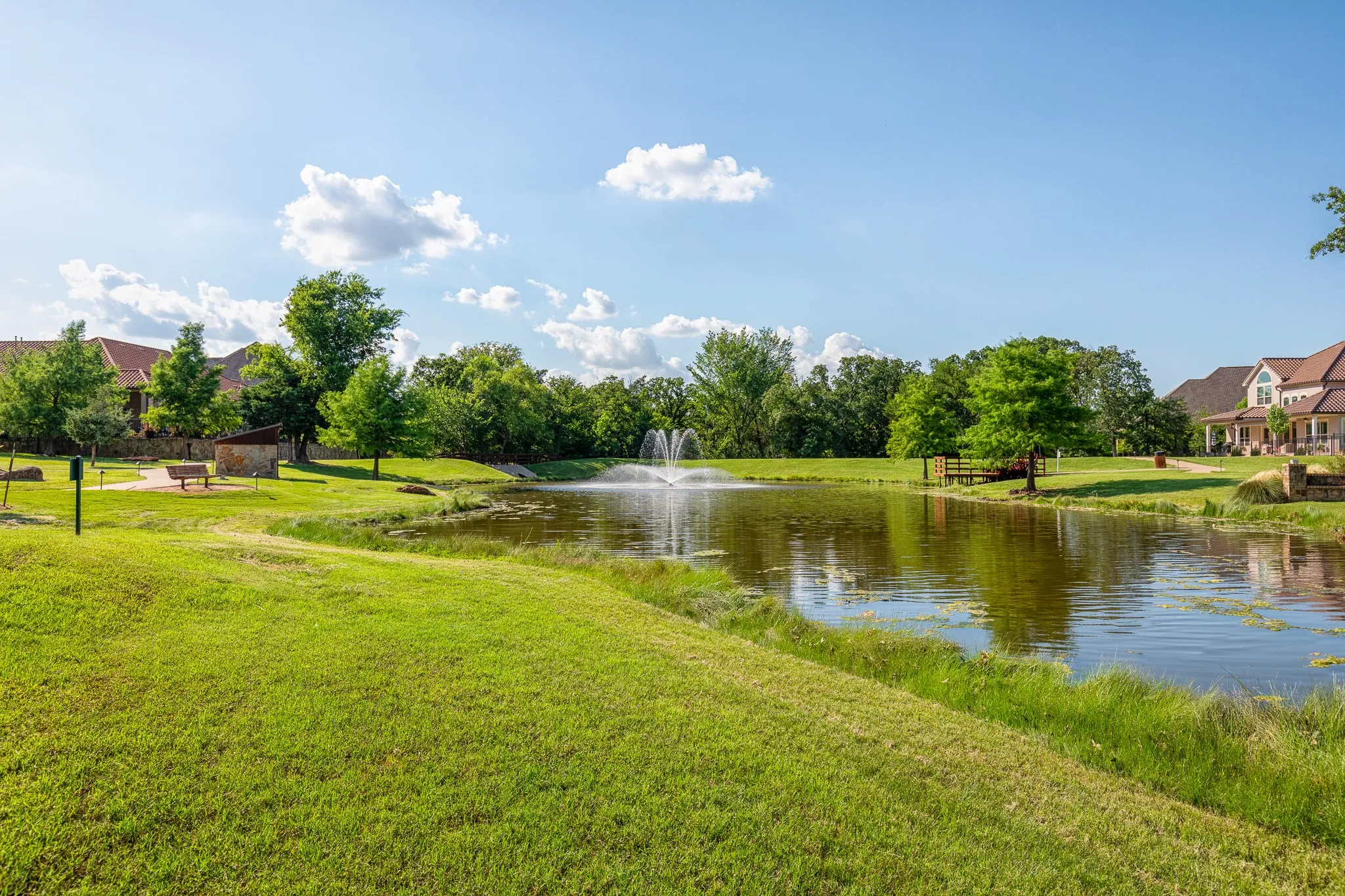 Expansive green space featuring a pond with a fountain, surrounded by mature trees