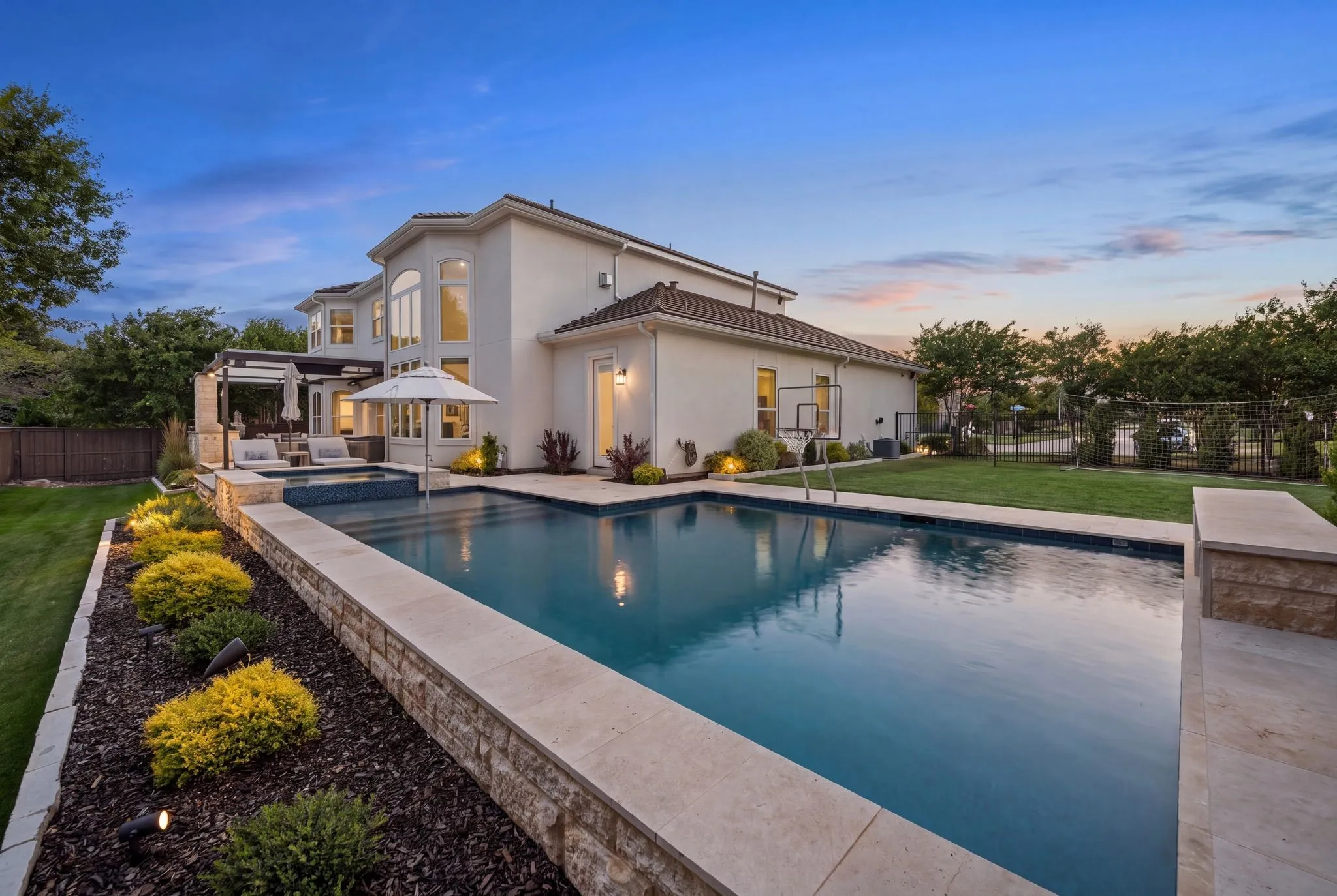 Stucco exterior with multiple windows, an in-ground swimming pool, an elevated spa, a covered patio area, and manicured landscaping