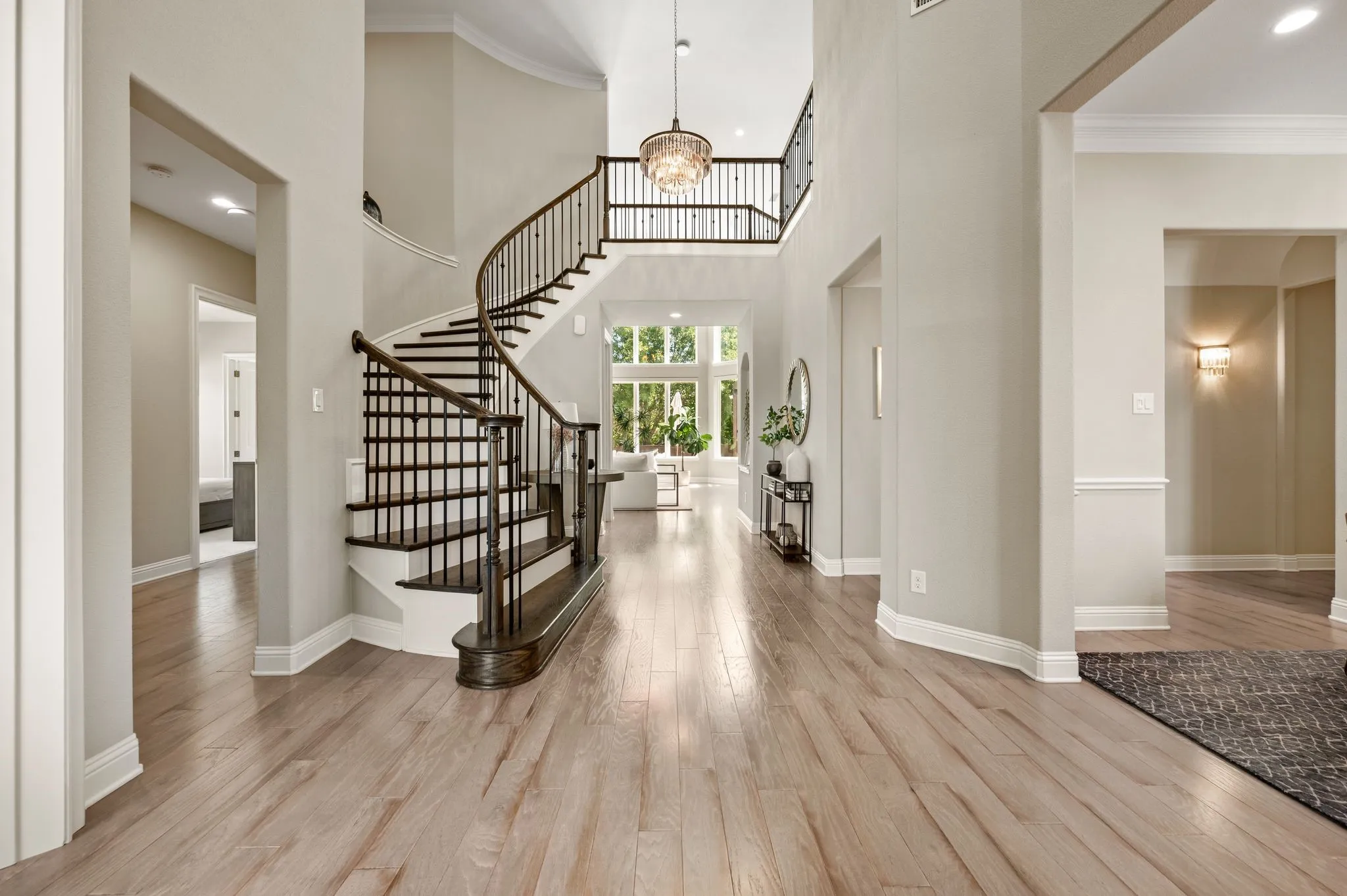 Grand foyer showcasing a dramatic spiral staircase with black metal railings, soaring two-story ceilings, and abundant natural light from multi-pane windows