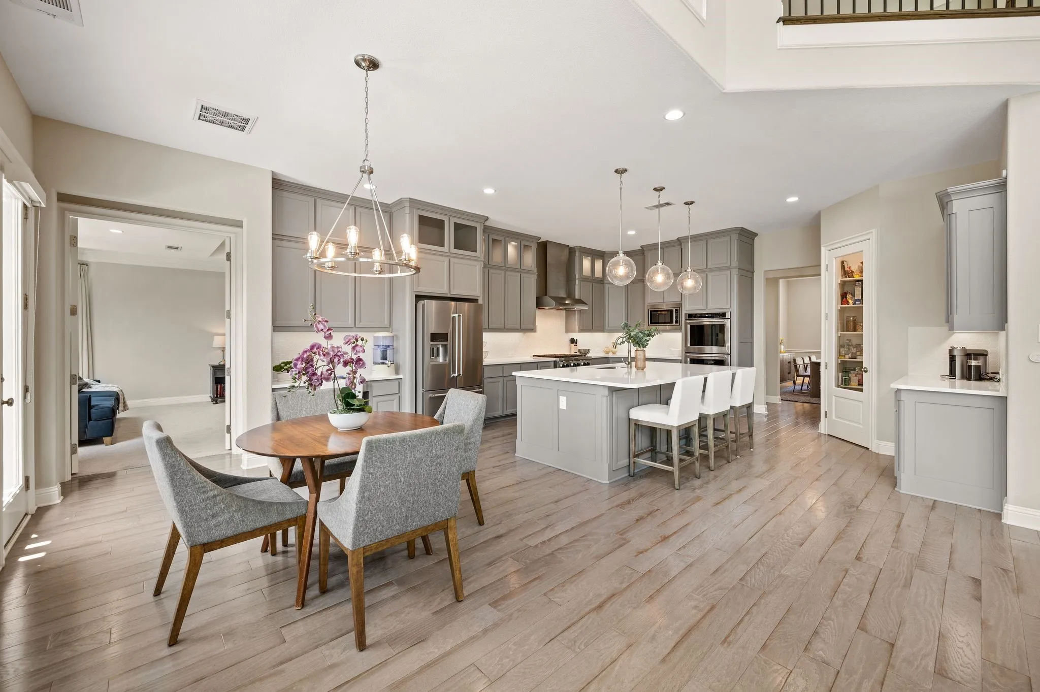 Open-concept kitchen and dining area featuring custom gray cabinetry, stainless steel appliances, white quartz countertops, a large center island with seating, and wood-finish flooring throughout