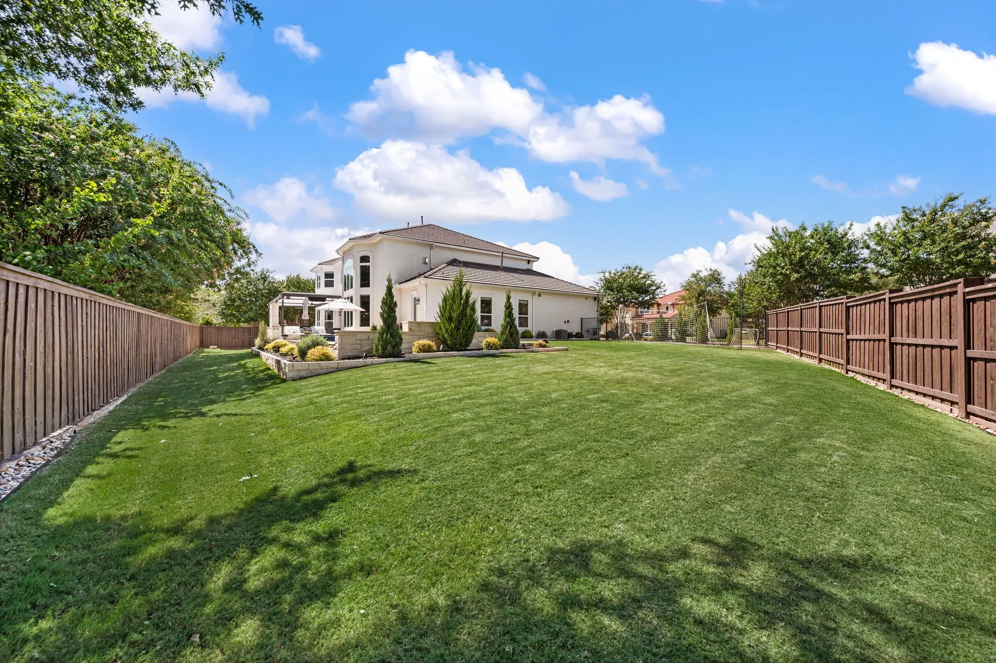 Expansive grassy yard with wood fencing, a patio area, and mature landscaping