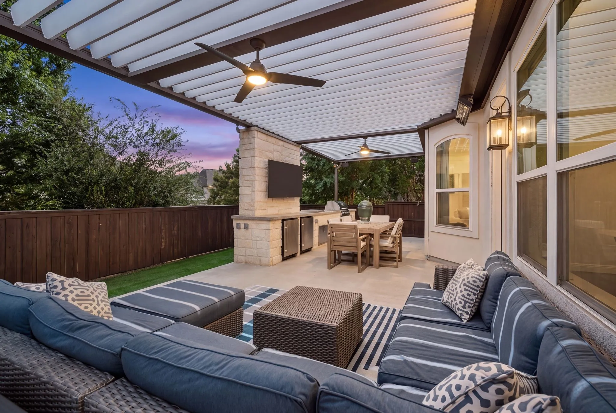 Expansive covered patio featuring a built-in outdoor kitchen, stone accent wall, ceiling fans, and an outdoor television