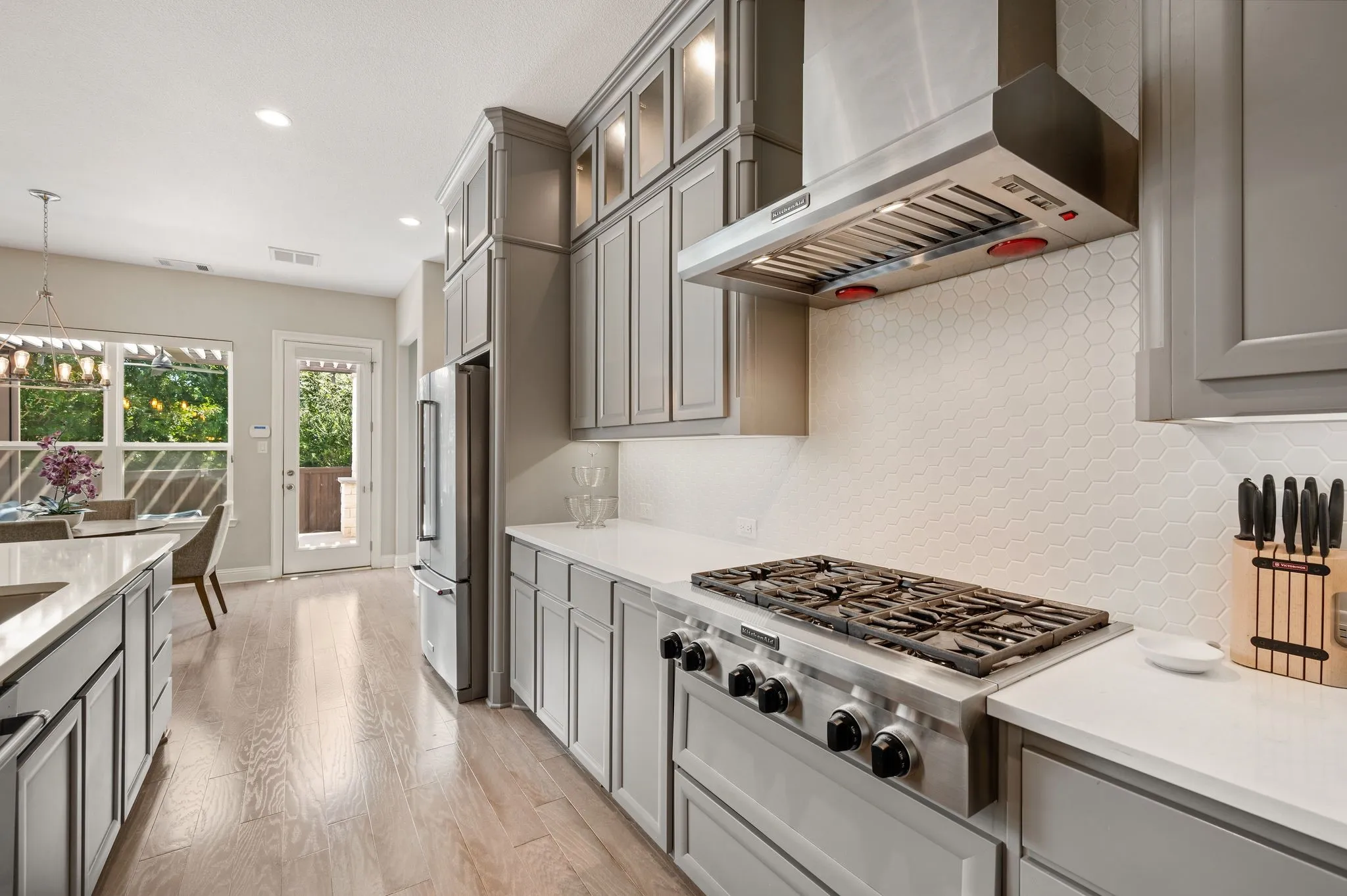 Chef's kitchen featuring custom cabinetry with contrasting trim, professional-grade six-burner gas cooktop with stainless steel hood, quartz countertops, and wood-finish flooring throughout the open layout