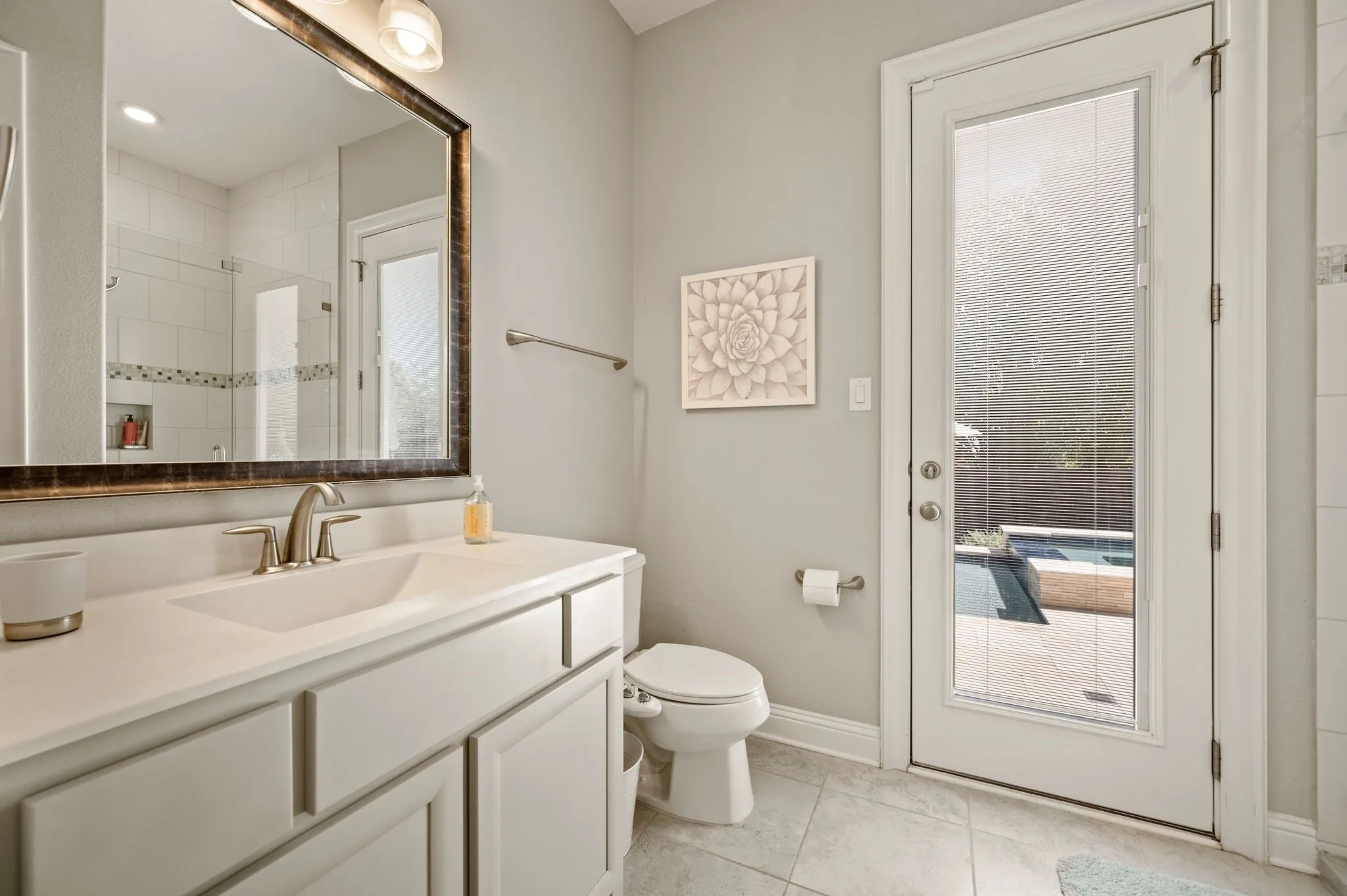 Spa-inspired primary bathroom featuring a framed mirror with bronze-finish hardware, white vanity cabinetry with brushed nickel fixtures, ceramic tile flooring, and a glass-enclosed shower enclosure