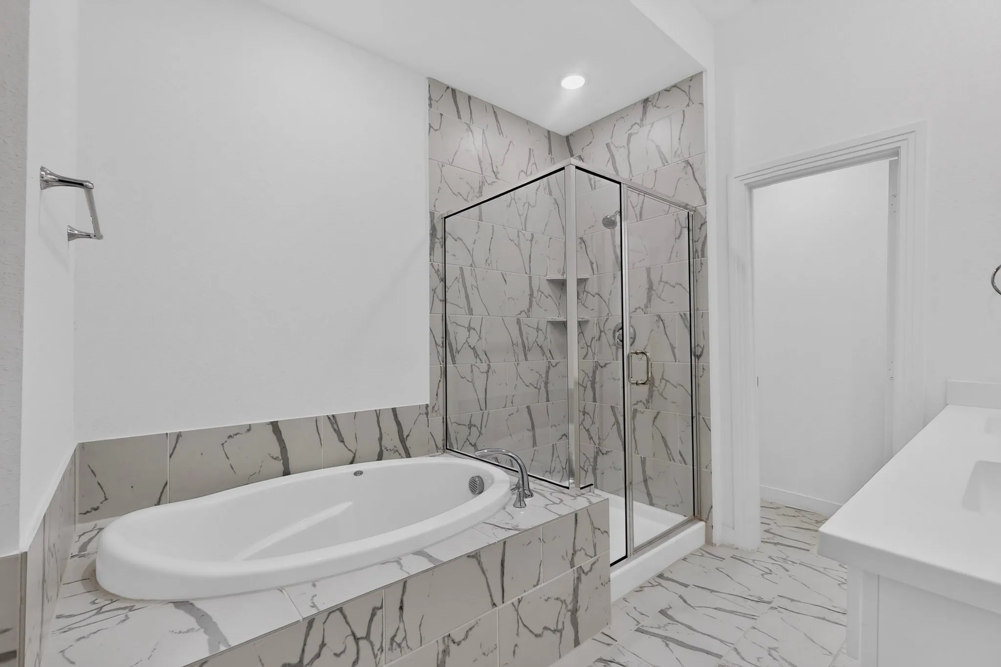Soaking tub with tiled surround, glass-enclosed shower with built-in niches, vanity with integrated sink, and large format tiled flooring