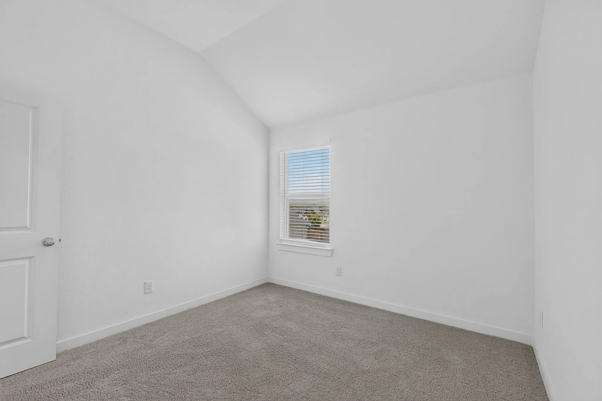 Vaulted ceiling accenting a neutral carpeted floor, white walls, and a single window with blinds