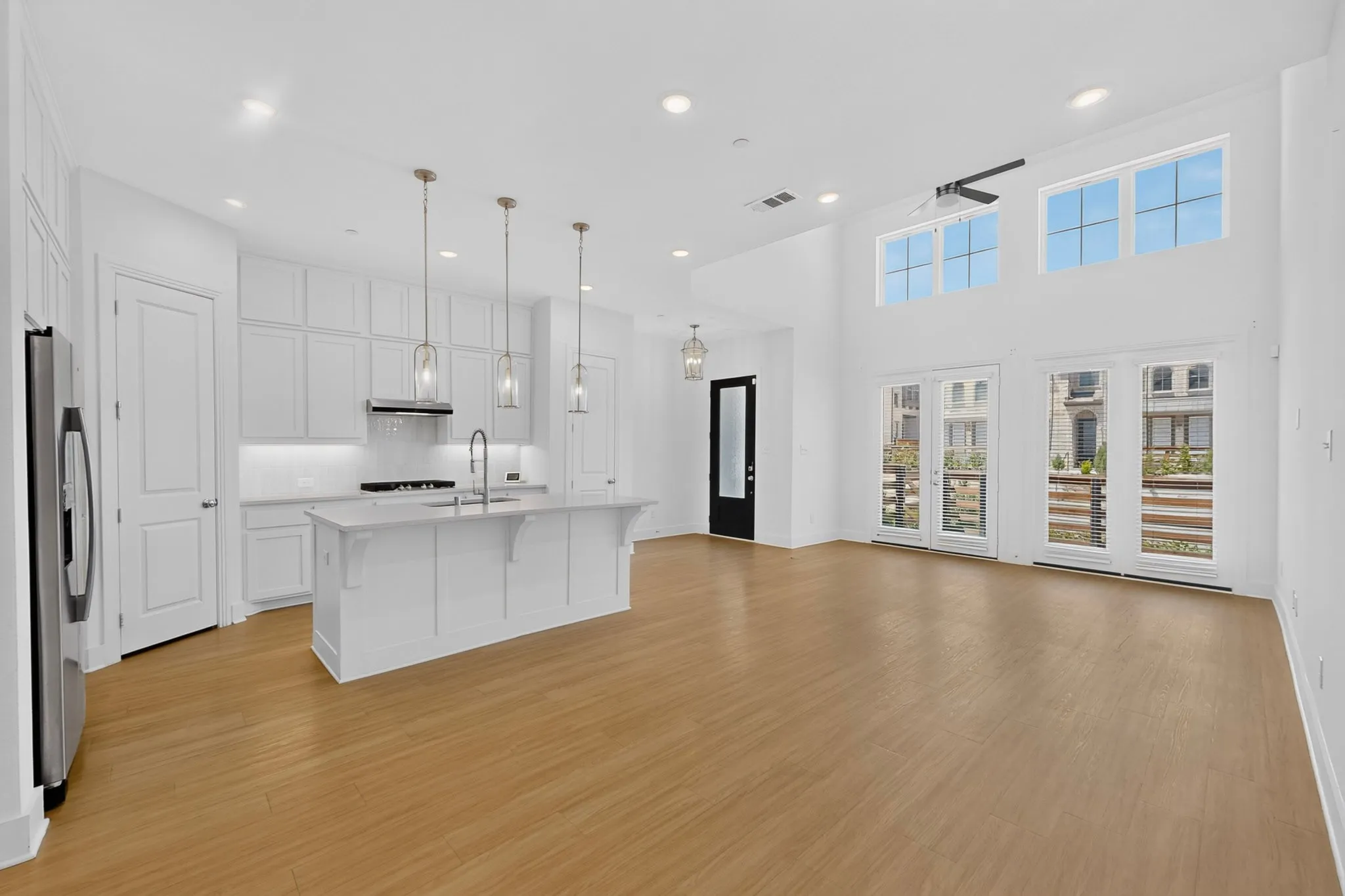 Open-concept layout featuring wood-finish flooring, a kitchen island with pendant lighting, white cabinetry, and high ceilings with transom windows