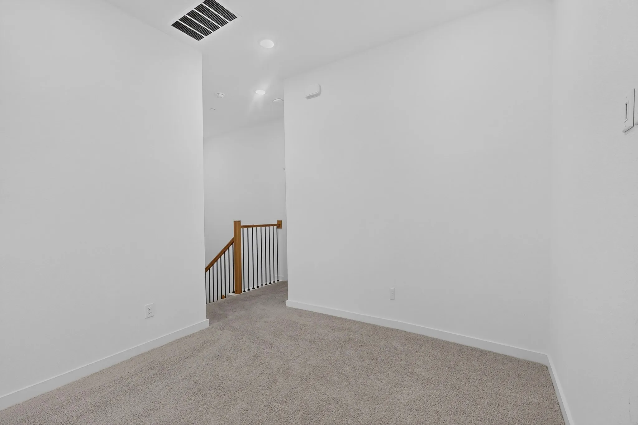 Carpeted flooring, recessed lighting, white walls, and wood-finish handrail with dark balusters