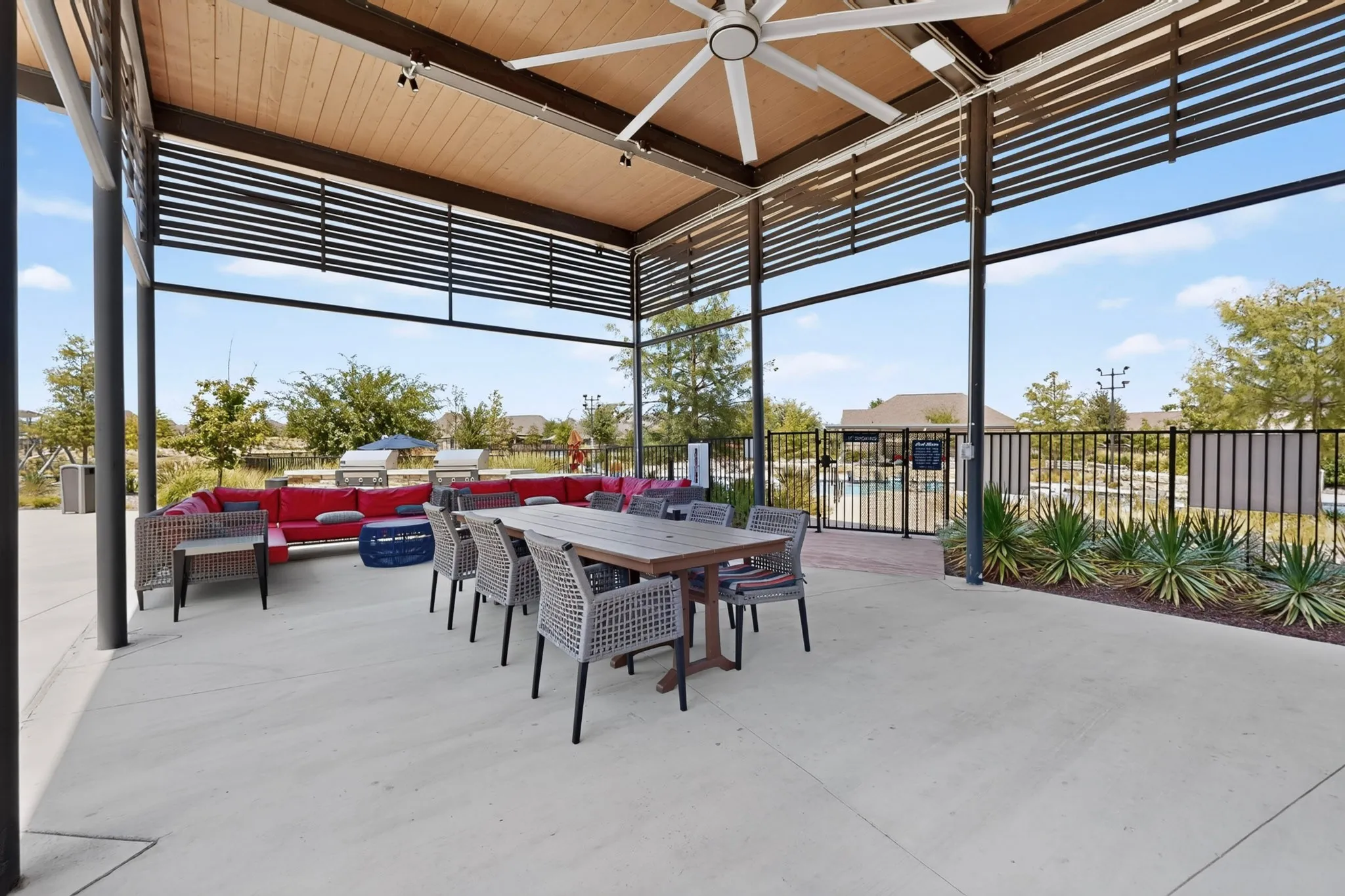 Covered outdoor patio with a wood-paneled ceiling, large ceiling fan, and concrete flooring