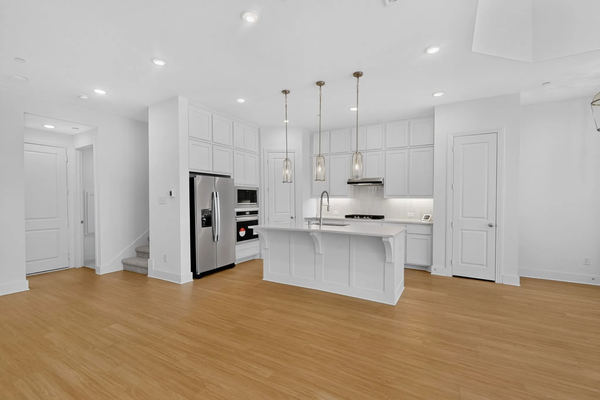 Open-concept kitchen featuring an island with a sink, white cabinetry, stainless steel appliances, and wood-finish flooring