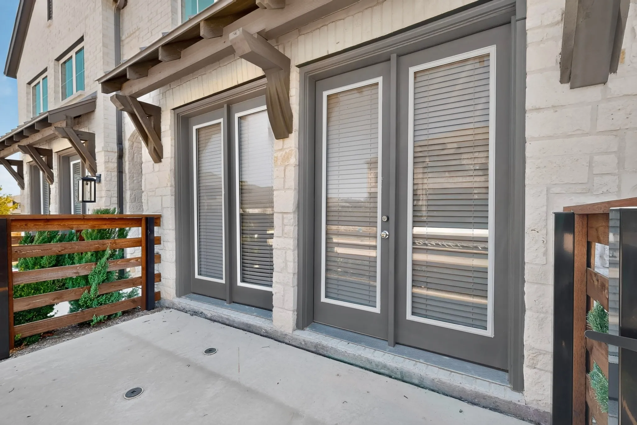 Stone-clad exterior featuring dual French doors, a concrete patio, a wood-slat privacy fence, and decorative overhead wood awnings