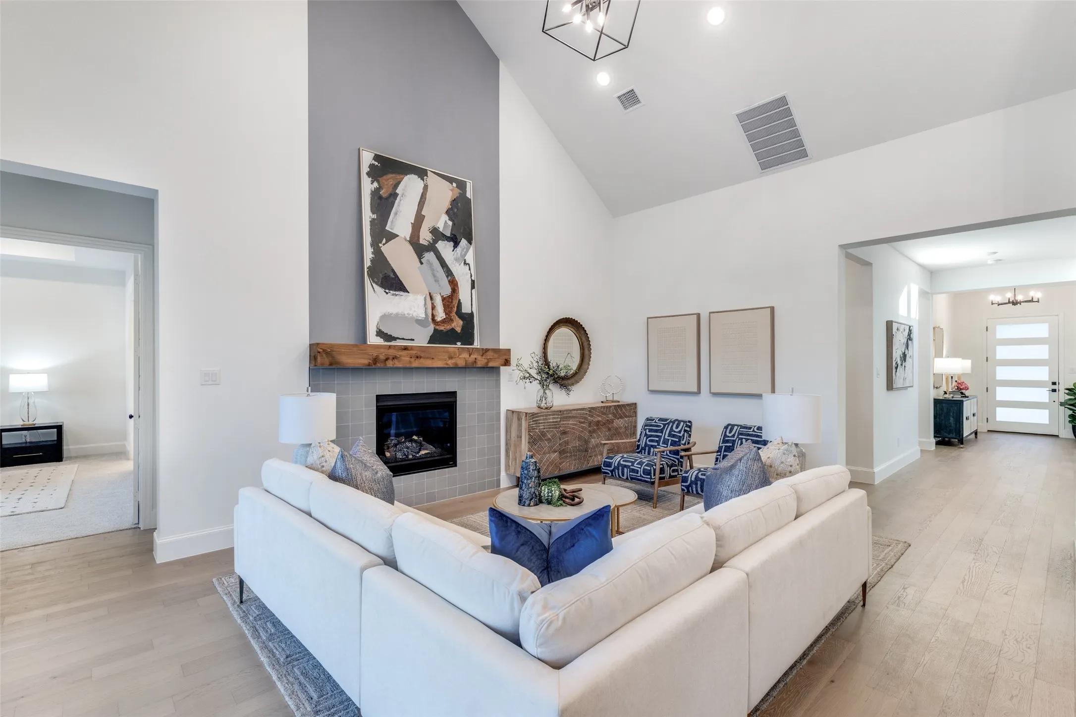 Living area with a chandelier, high vaulted ceiling, light wood-style flooring, and a glass covered fireplace