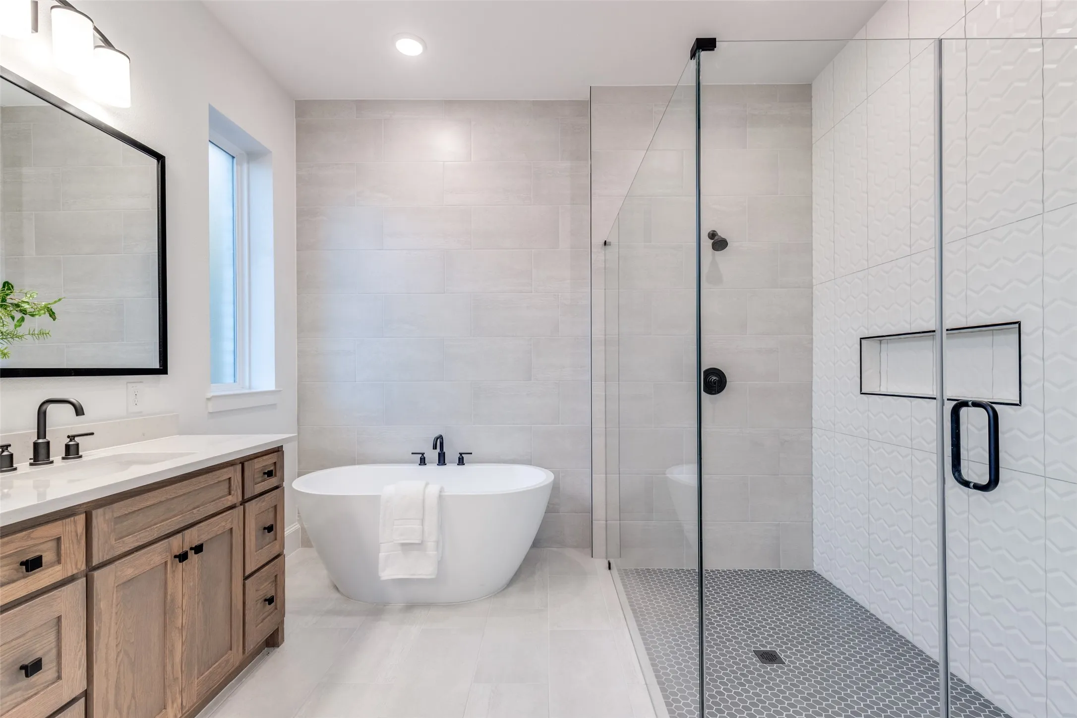 Spa-like primary bathroom with a freestanding bath, a large walk-in shower, double vanity, tile walls, and recessed lighting