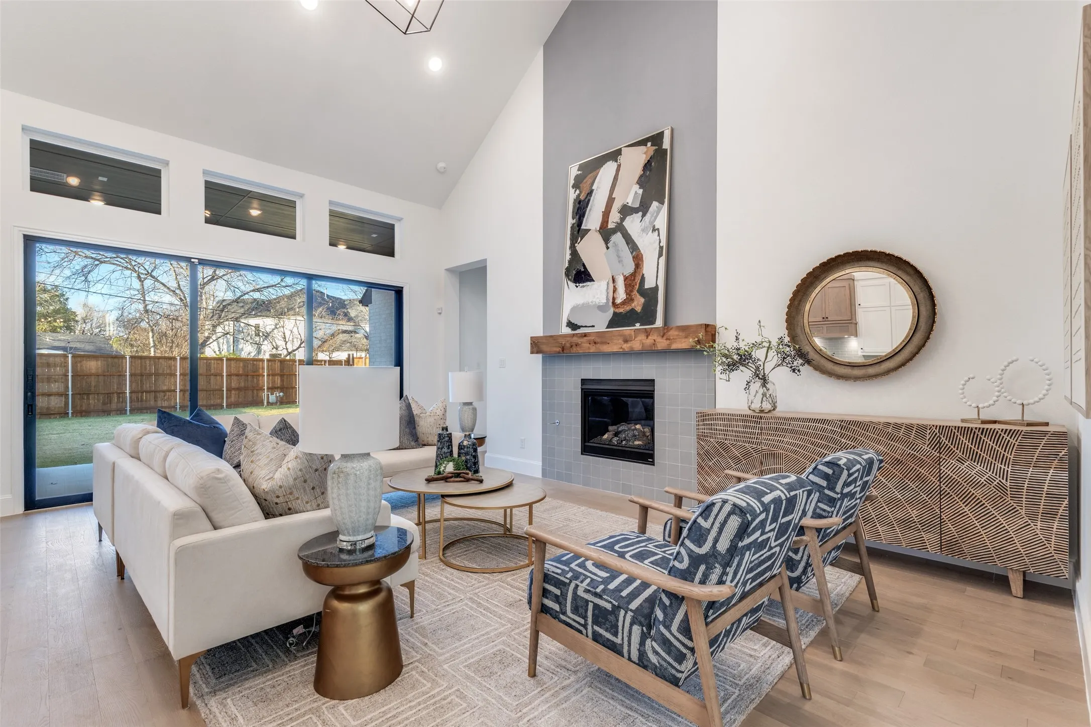 Living area with light wood-type flooring, high vaulted ceiling, and a tiled fireplace