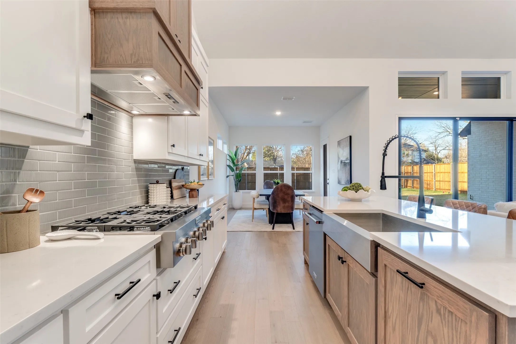 Kitchen featuring light stone counters, white cabinetry, brown cabinetry, stainless steel appliances, and light wood-type flooring