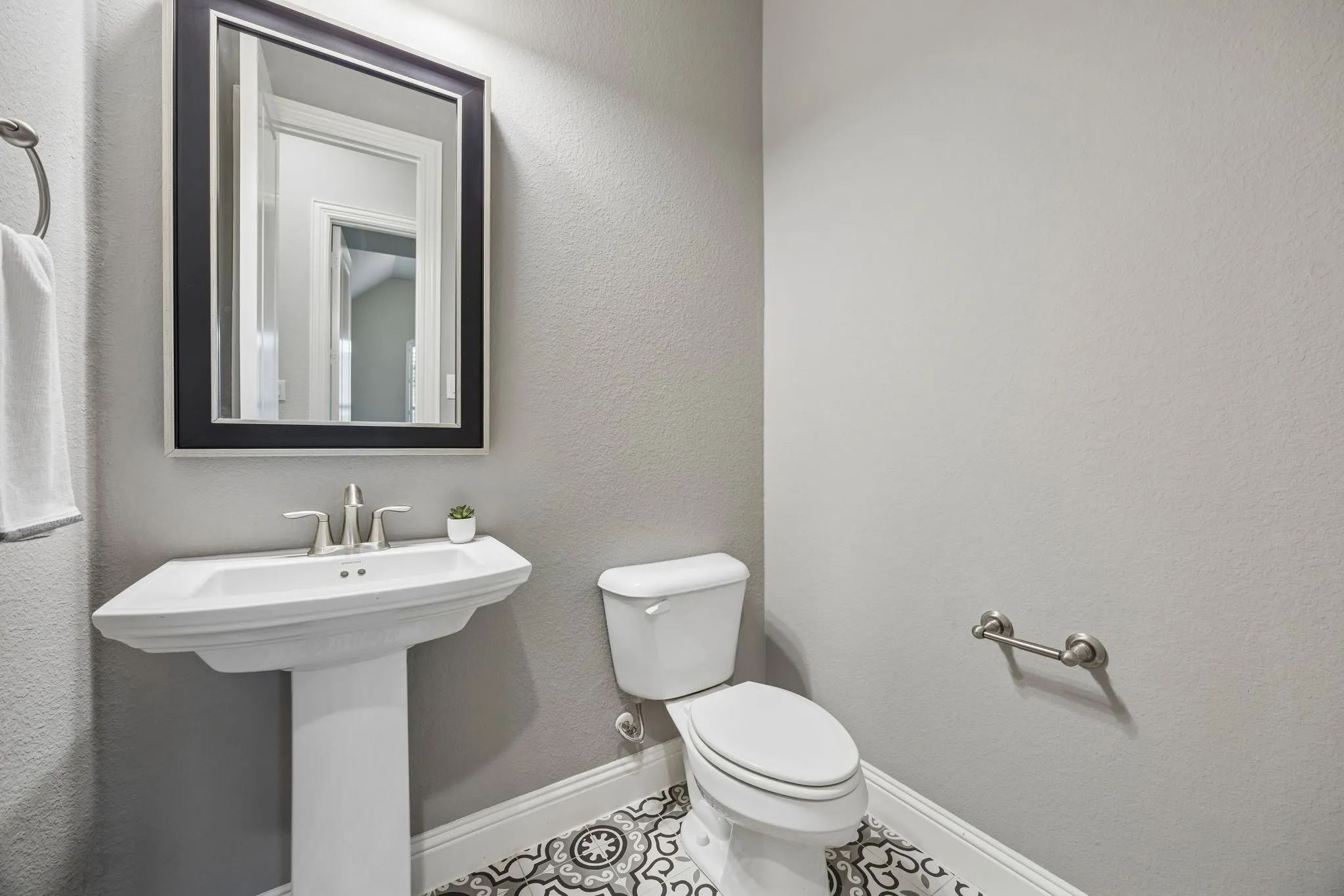 Pedestal sink with a polished chrome faucet, framed mirror, and decorative tile flooring