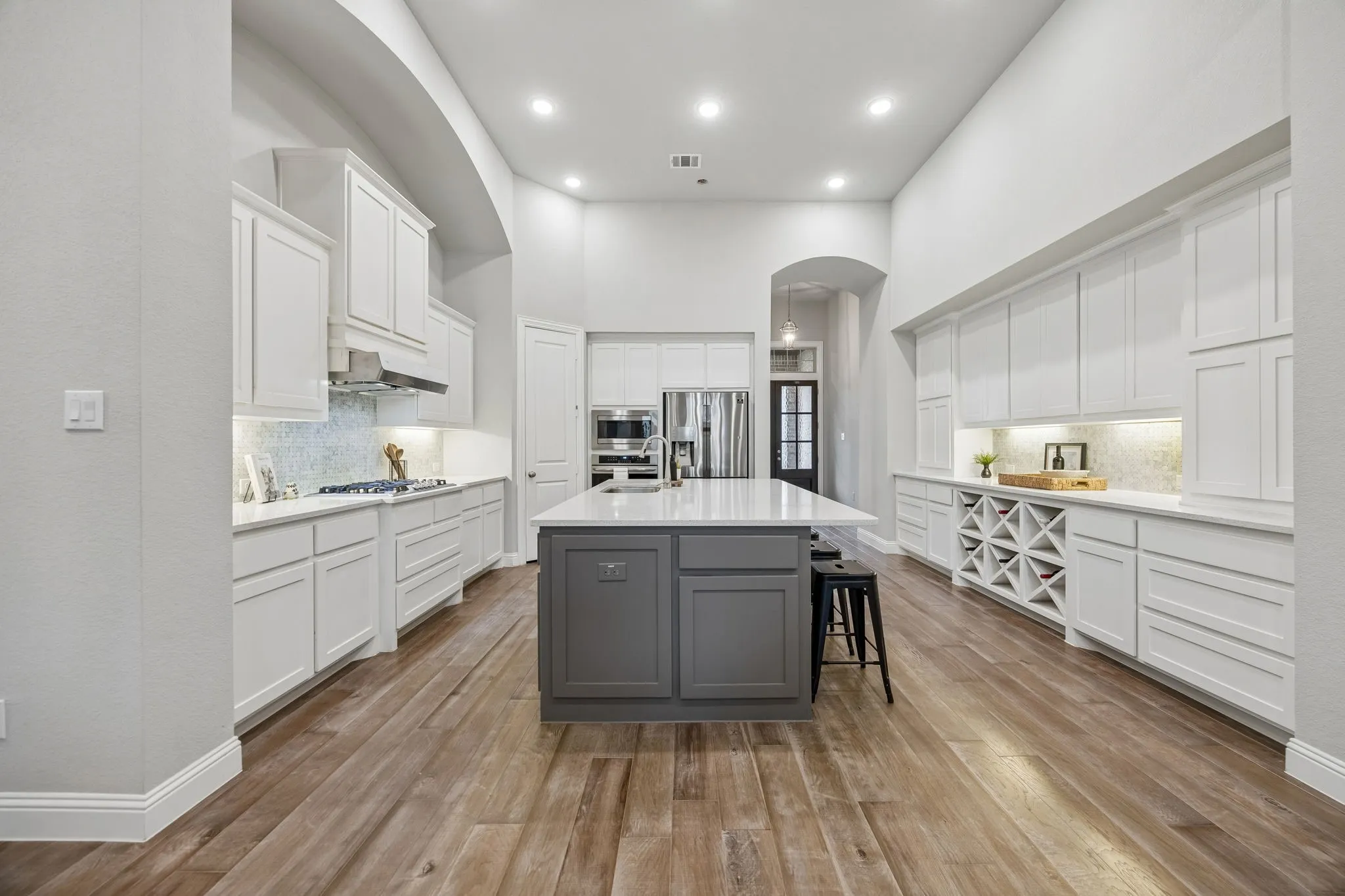 Spacious kitchen with a central island, wood-finish flooring, white cabinetry, and built-in wine storage