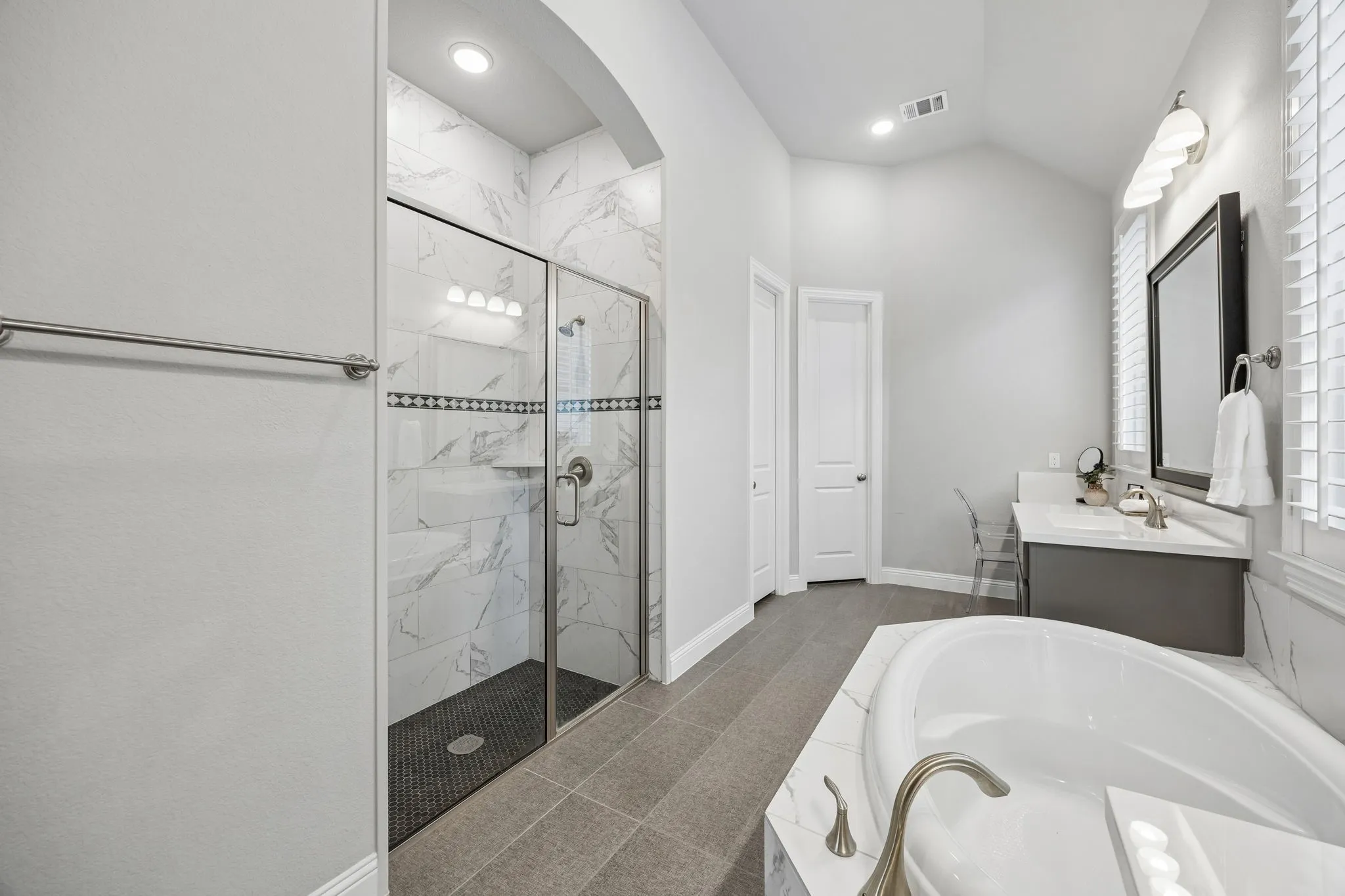 Recessed lighting illuminates a glass-enclosed shower with tiled walls and a dark tiled floor