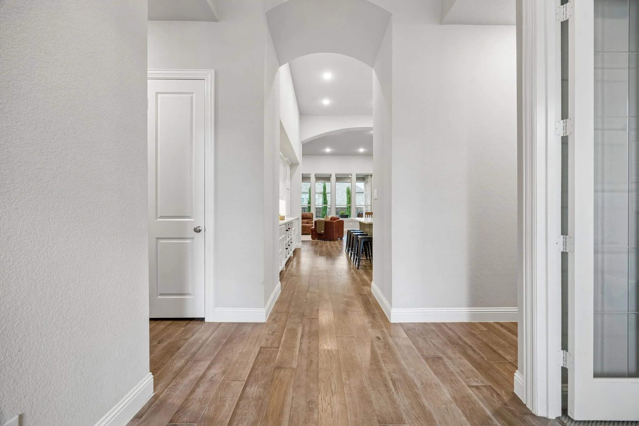 Wood-finish flooring, recessed lighting, arched entryway, white interior doors, and crisp white trim