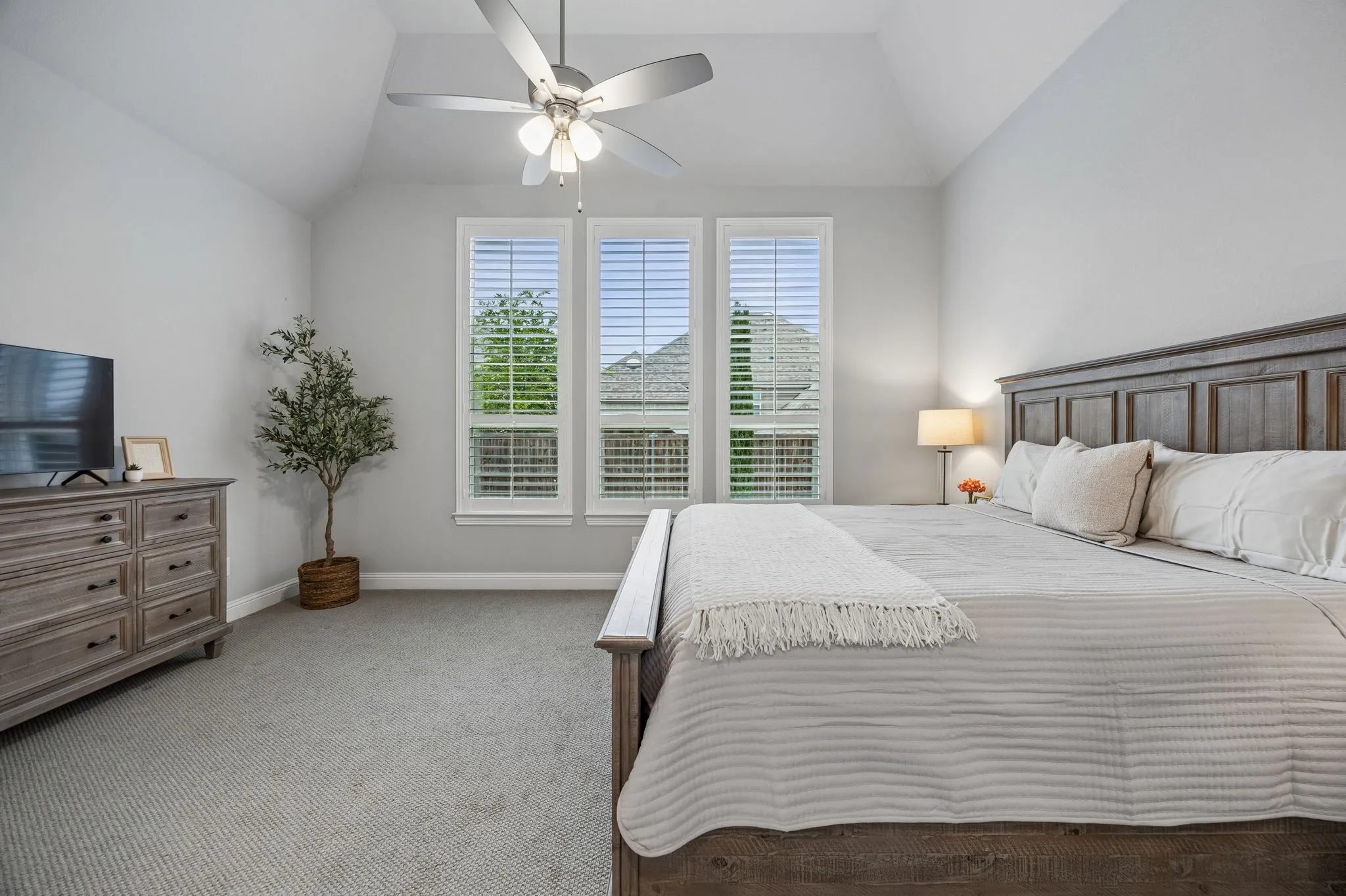 Vaulted ceiling with a ceiling fan, three windows with plantation shutters, light gray wall paint, and gray carpet flooring