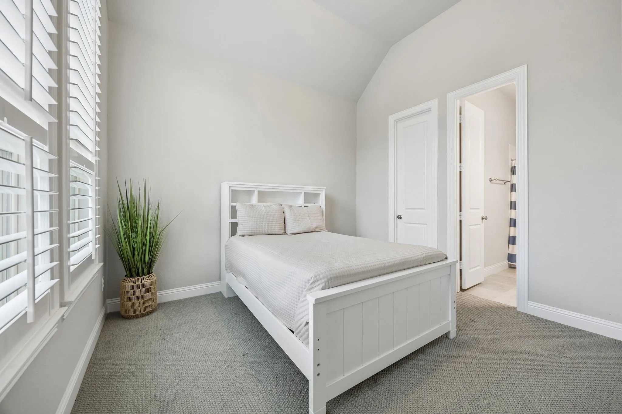 Vaulted ceiling, plantation shutters, grey carpeting, white trim, and an attached bathroom with tiled flooring