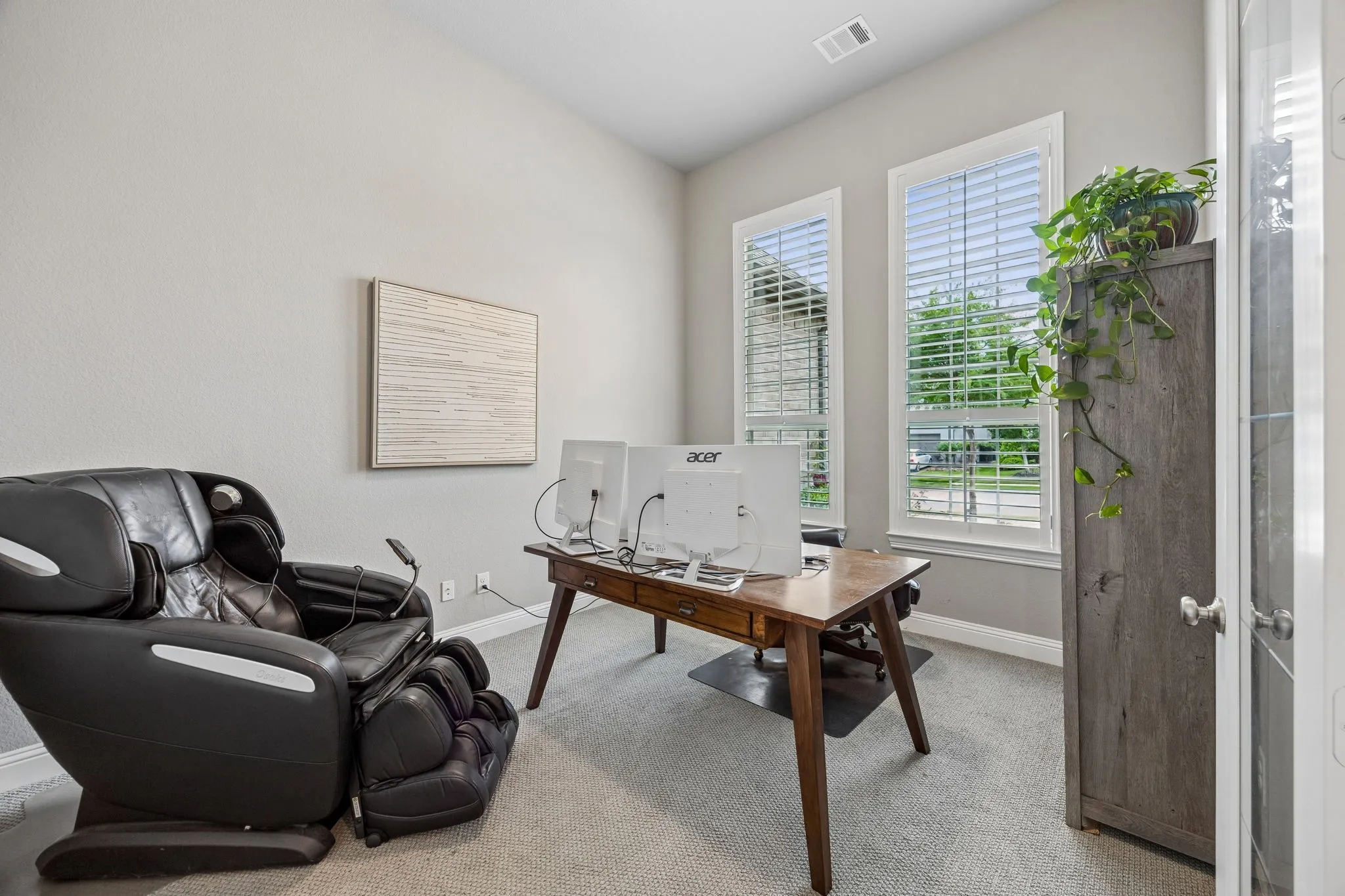 Neutral wall paint, two tall windows with white plantation shutters, and light-colored carpeting