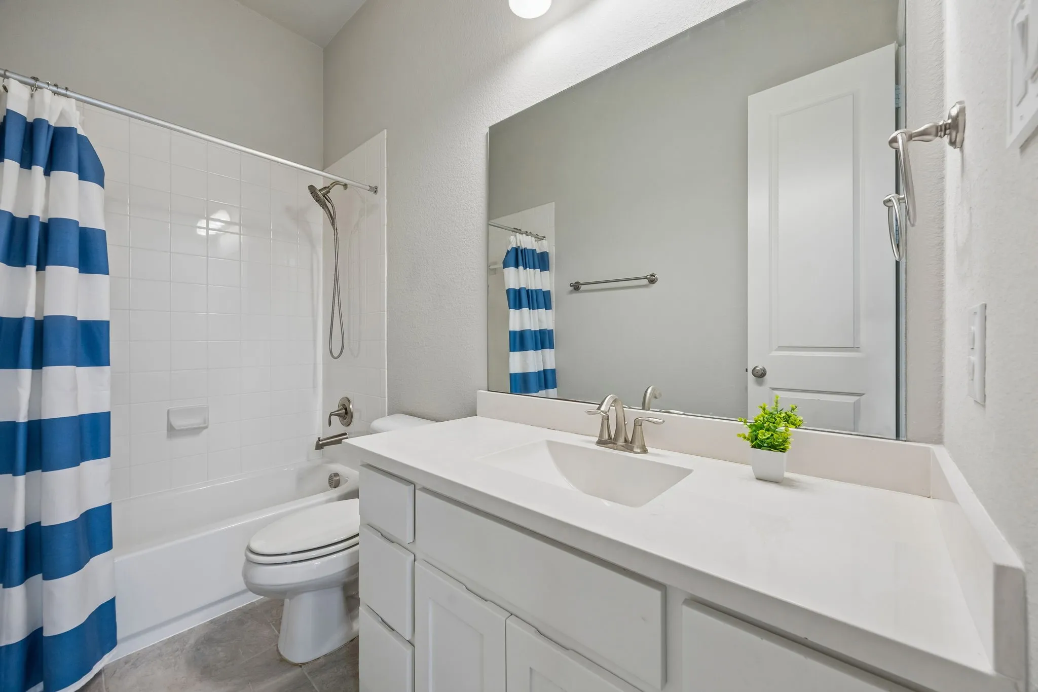 White vanity with integrated sink, brushed nickel faucet, large wall-mounted mirror, and white tiled shower-tub combination