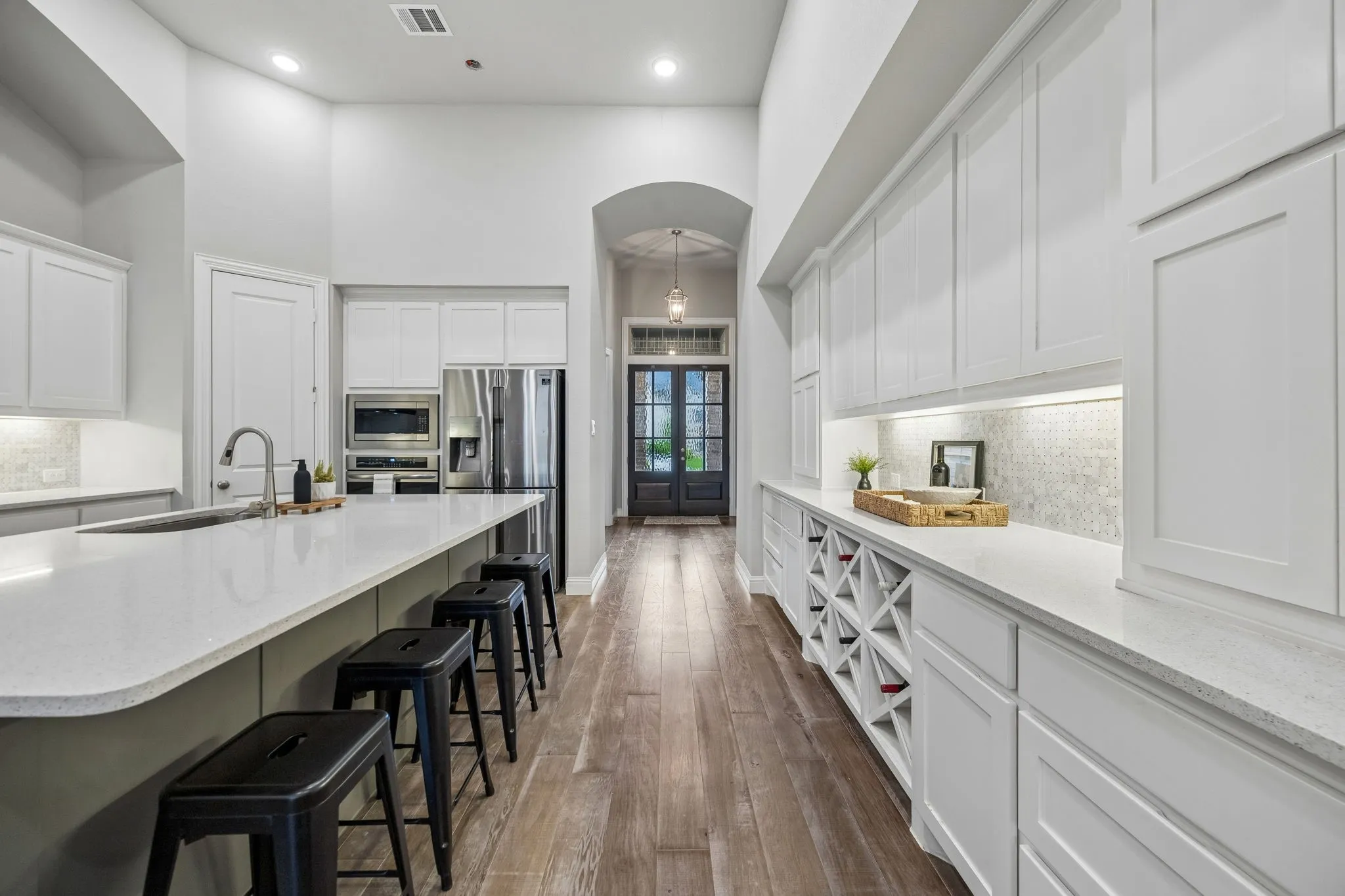 Expansive kitchen island with an undermount sink, stainless steel appliances, extensive white cabinetry, quartz countertops, and wood-finish flooring