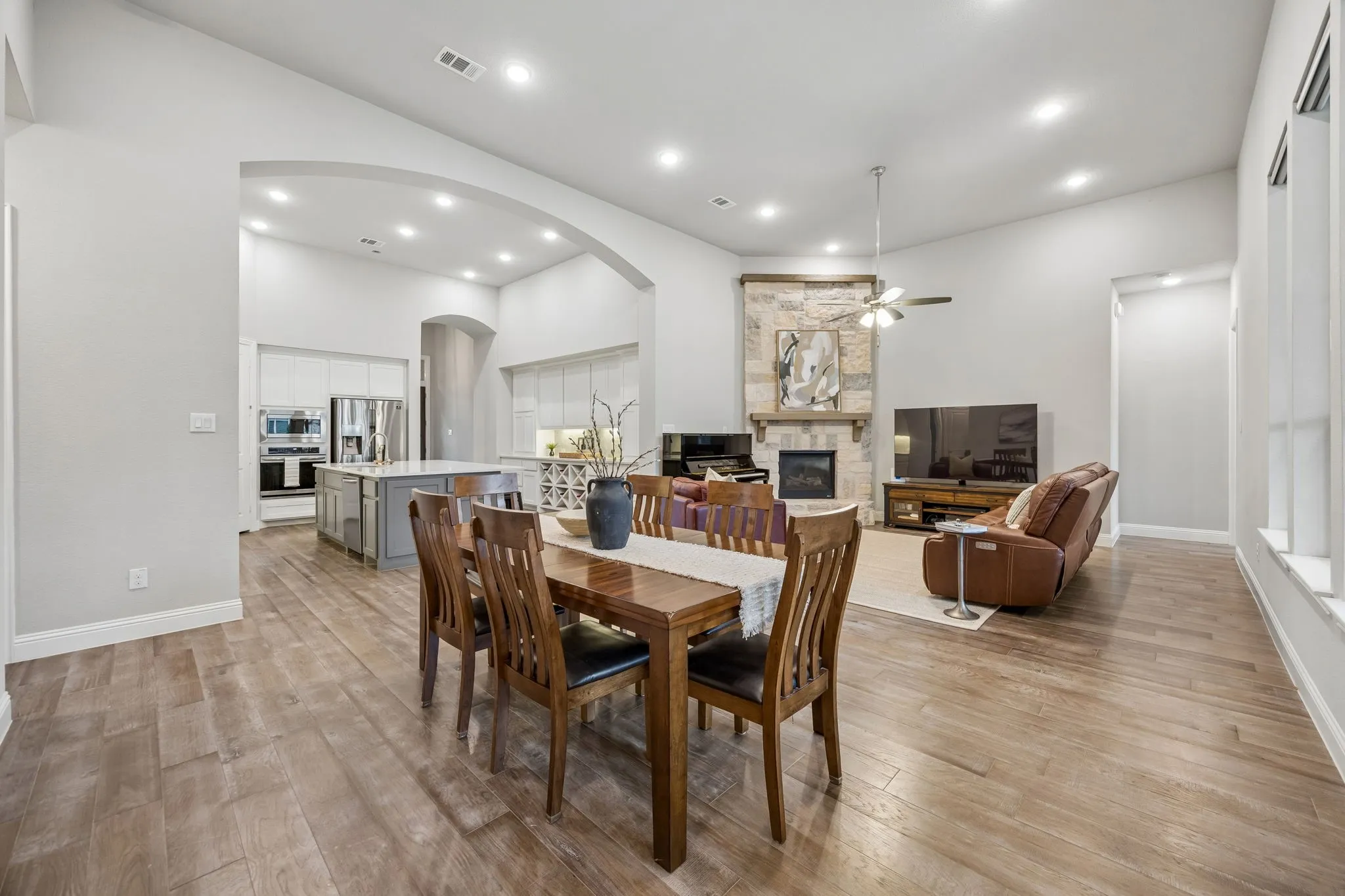 Wood-finish flooring throughout, arched entryway, fireplace with stone surround, recessed lighting, and a ceiling fan