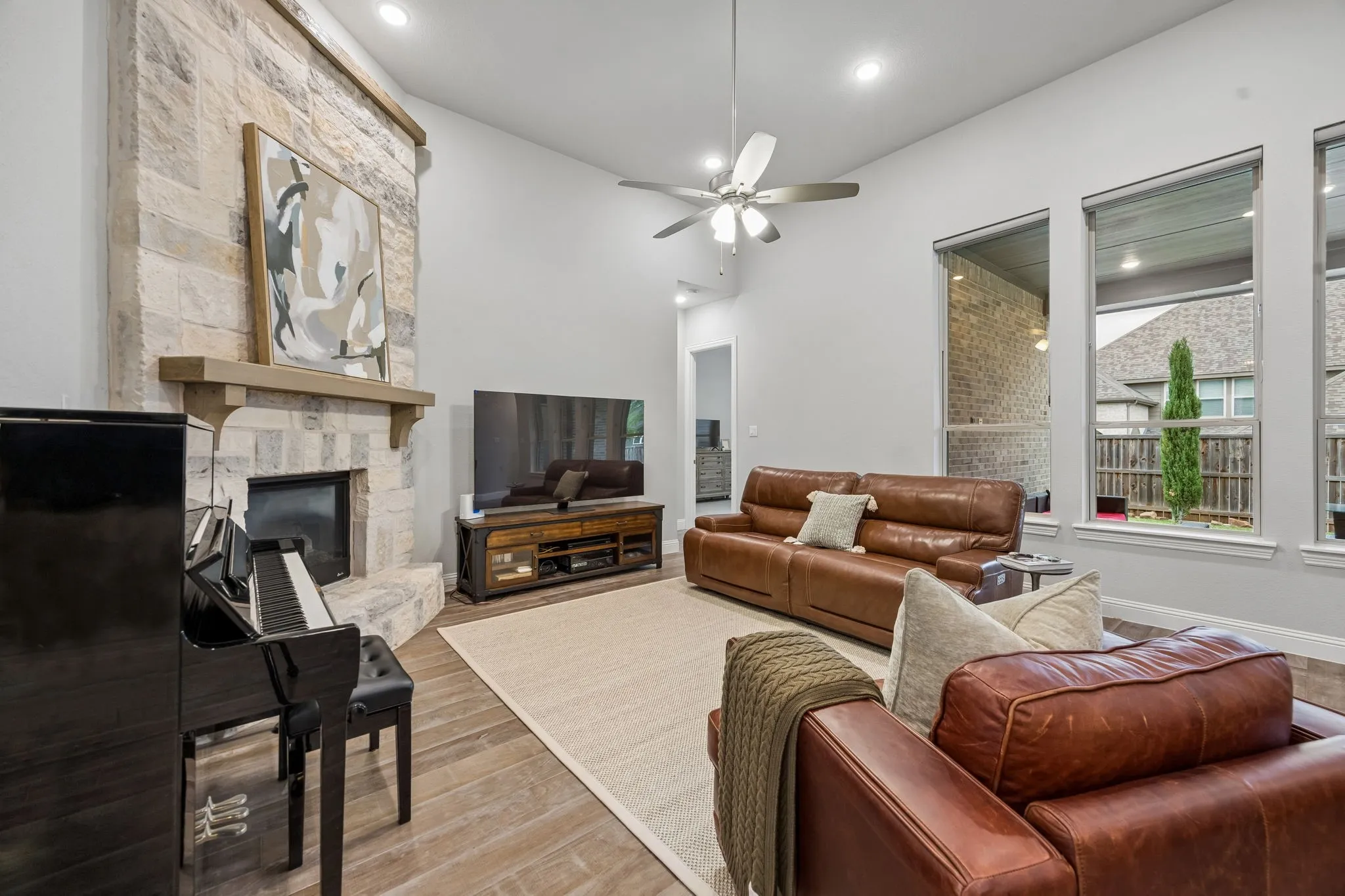 Vaulted ceilings with recessed lighting, ceiling fan, stone-front fireplace with wood mantel, wood-finish flooring, and multiple vertical windows