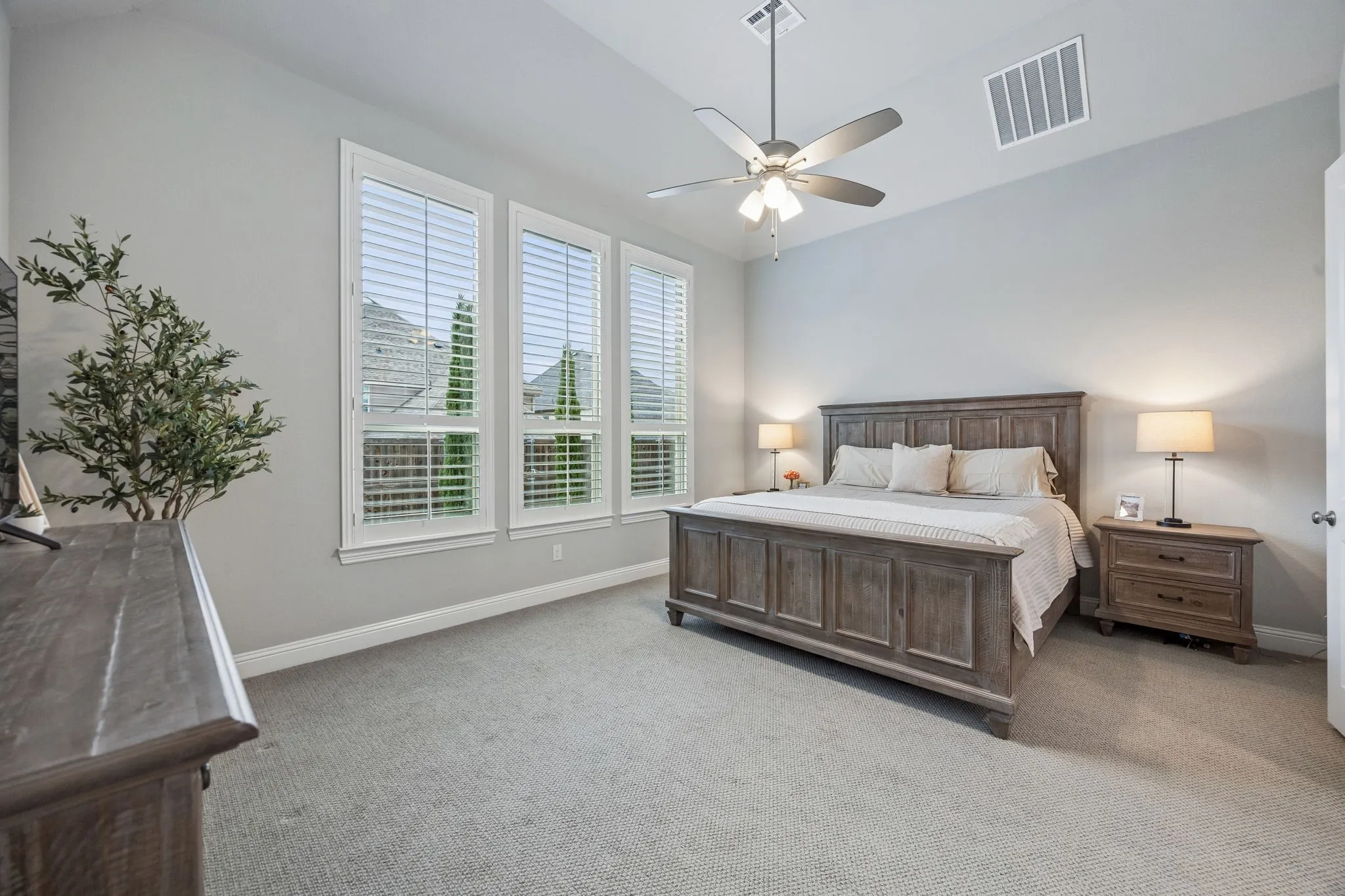 Vaulted ceiling, ceiling fan, three windows with plantation shutters, light gray wall paint, and gray carpet flooring