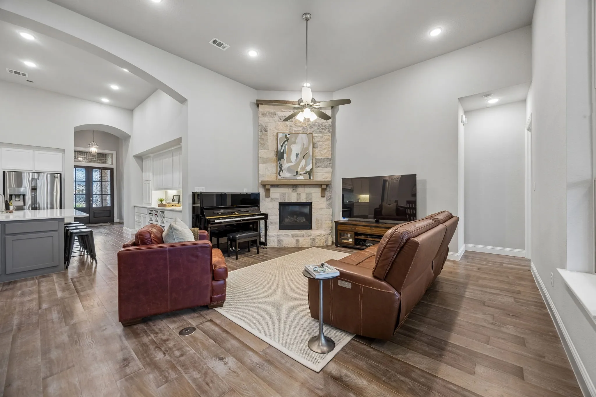 Vaulted ceilings, wood-finish flooring, stone fireplace with a wood mantle, recessed lighting, and a ceiling fan