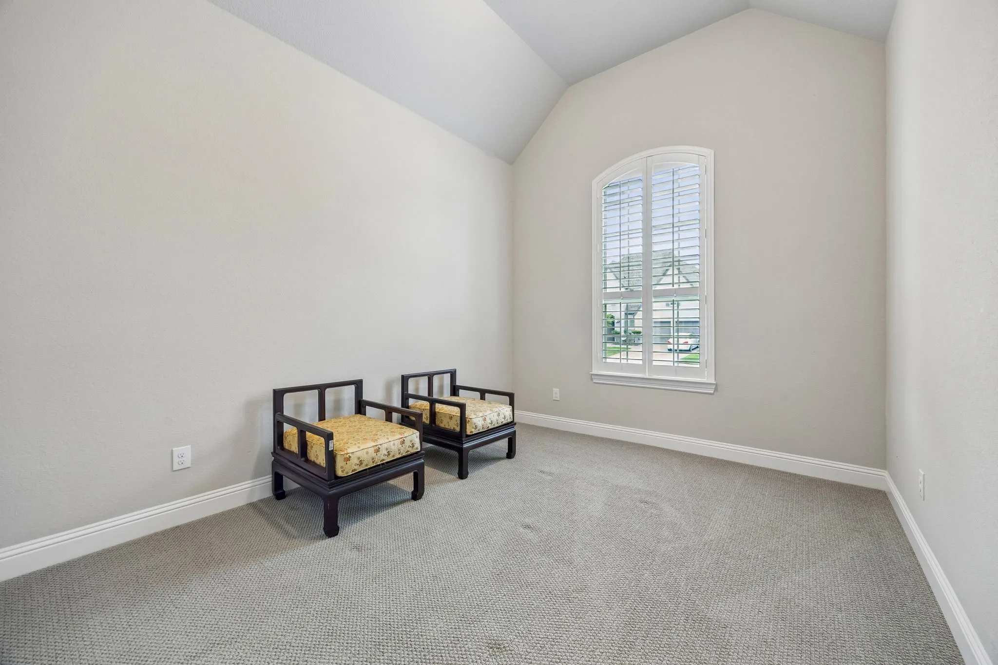 Vaulted ceiling, arched window with plantation shutters, light gray wall tones, and gray carpeting