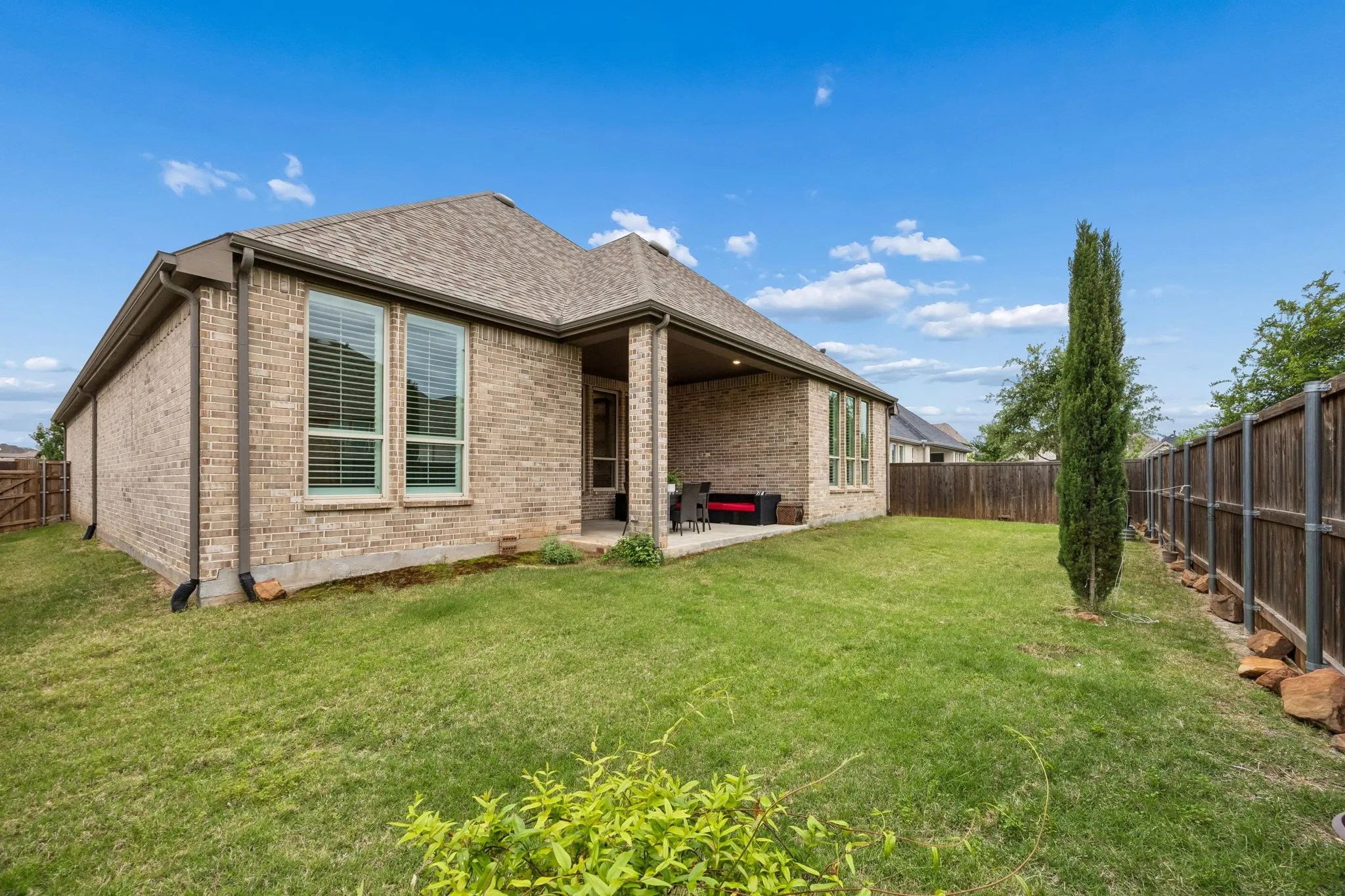 Brick exterior with a covered patio, fenced backyard, and a manicured lawn