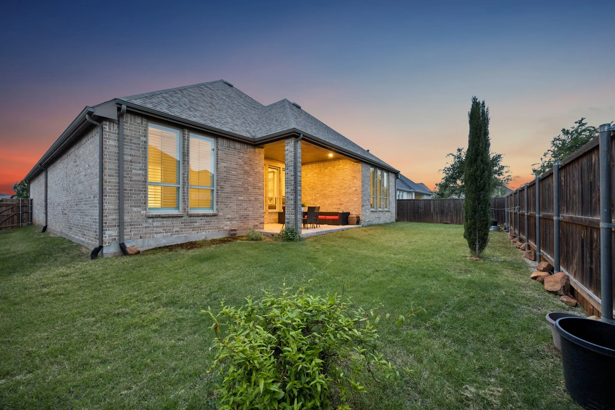 Expansive backyard featuring a manicured lawn, full brick exterior, covered patio, privacy fencing, and double-pane windows