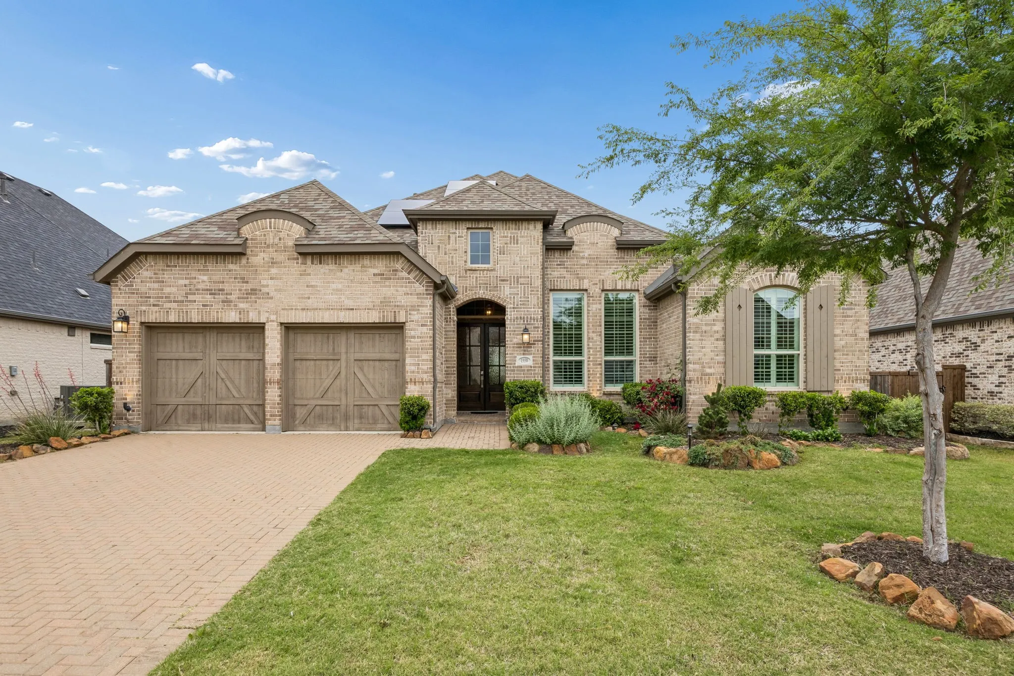 Brick exterior with stone accents, arched entry, two-car garage with wood-look doors, and a paver driveway