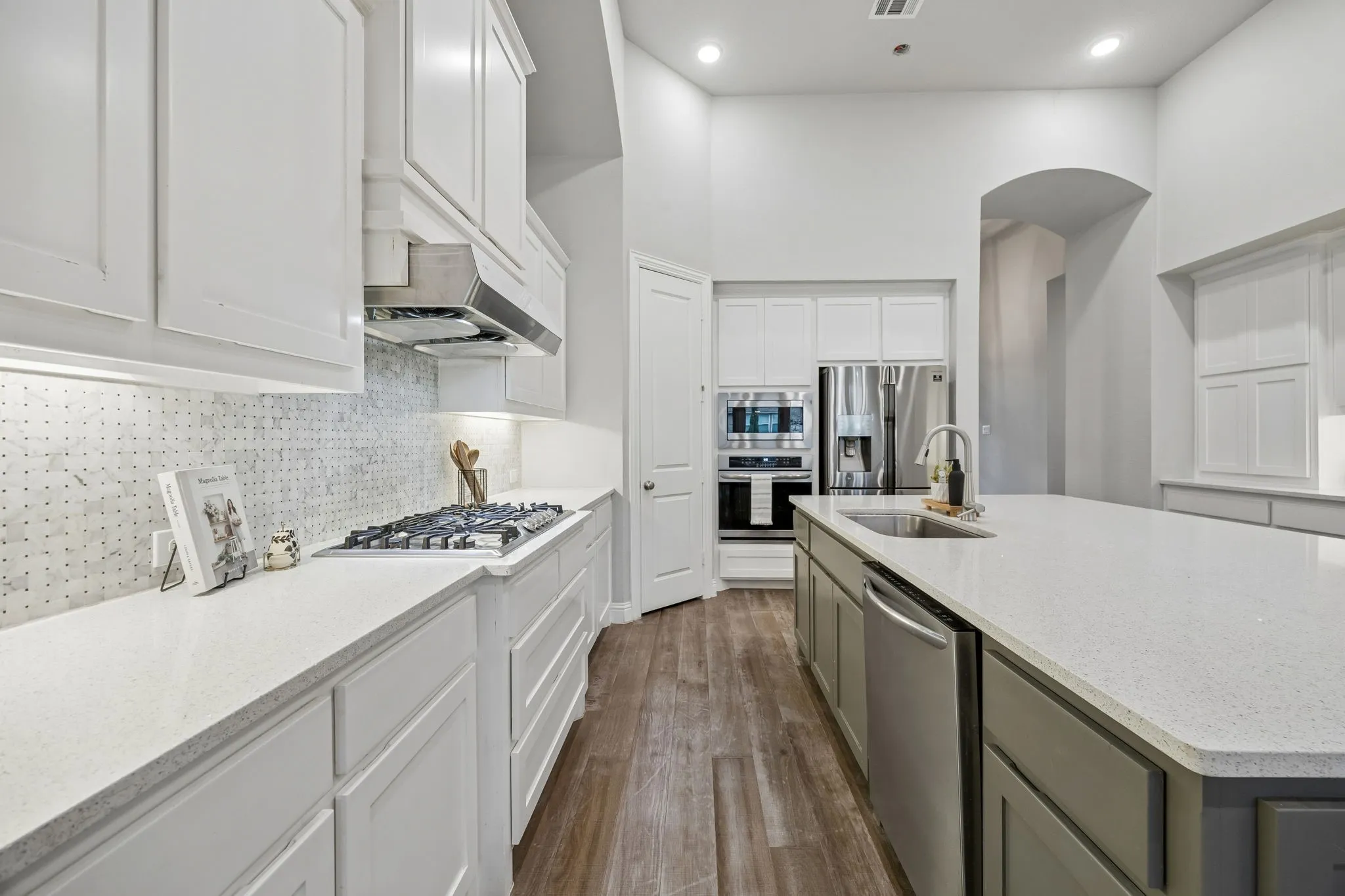 Stainless steel appliances, recessed lighting, wood-finish flooring, white cabinetry, and a kitchen island with sink