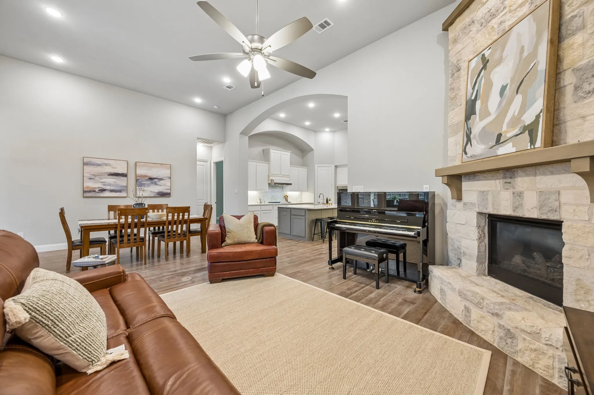 Spacious living area featuring a stone-clad fireplace with mantel, vaulted ceiling with a ceiling fan, recessed lighting, and wood-finish flooring